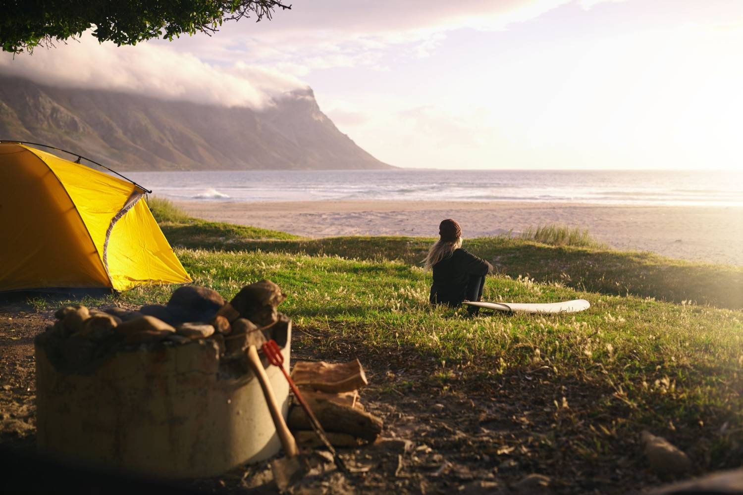 A tent pitched above a beach, two people sitting in the evening light