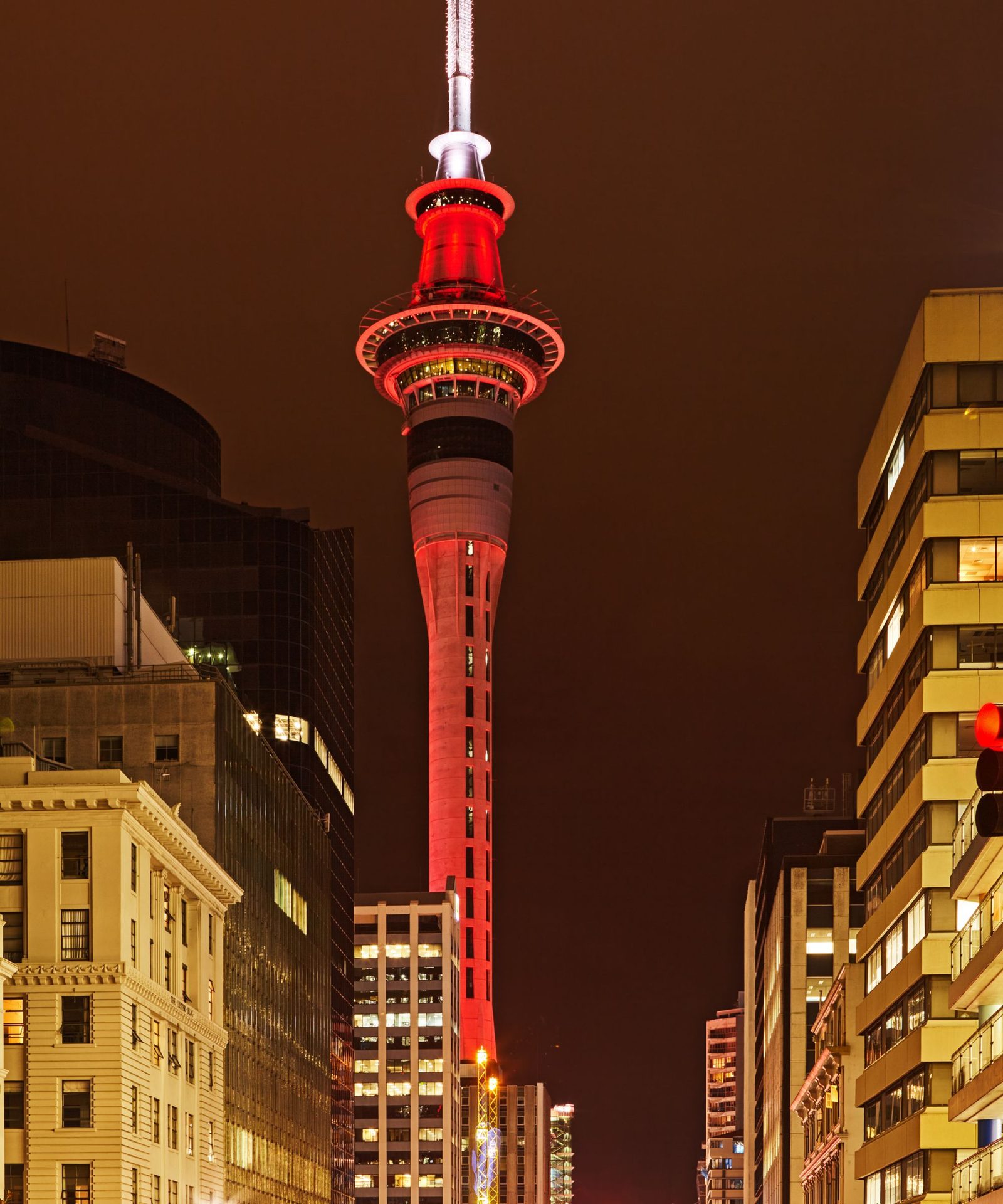 The Sky Tower lit red at night between city buildings