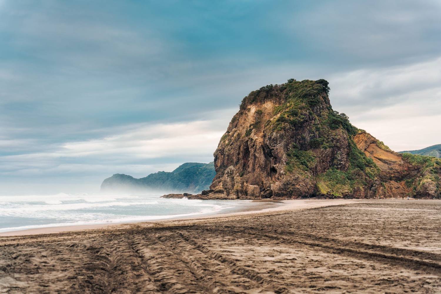 Black sand and a dramatic headland on Auckland's west coast at dusk