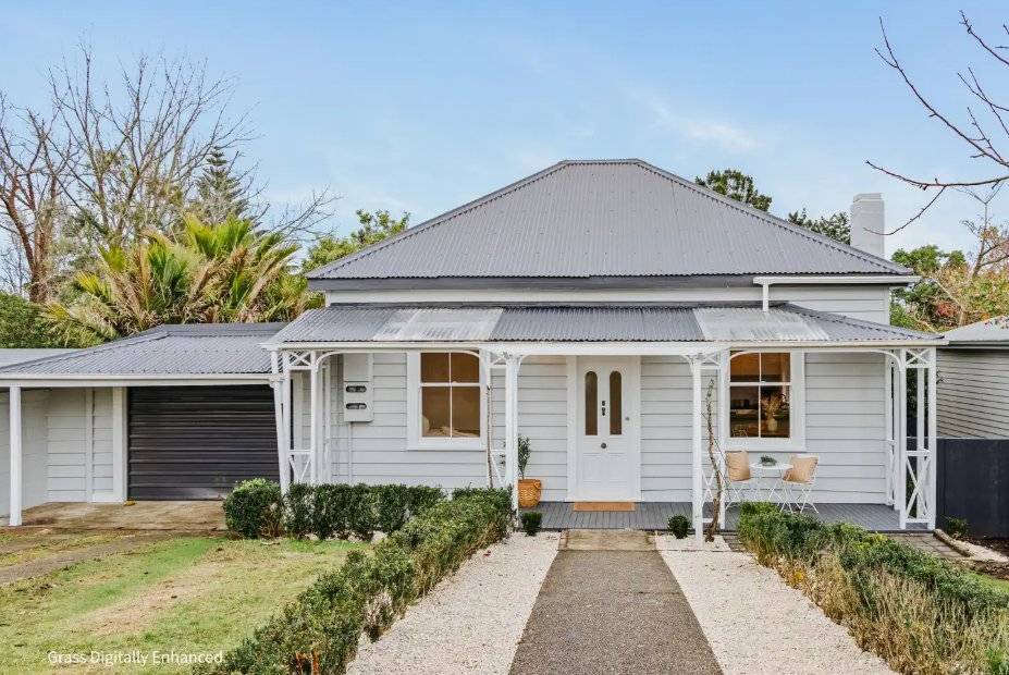 A restored white weatherboard villa with a verandah and clipped hedges on a sunny Tauranga street