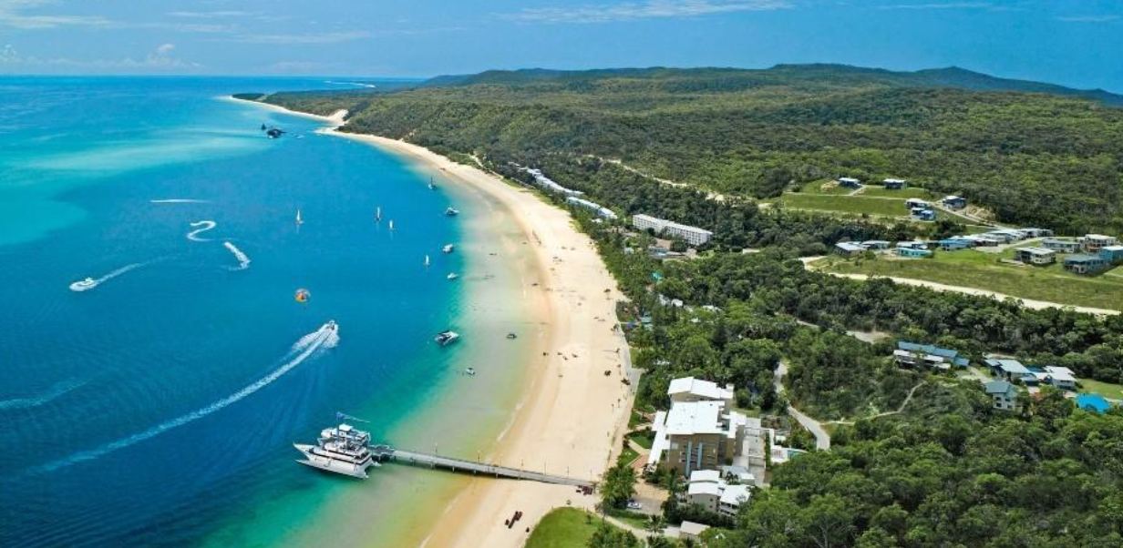 Turquoise water and a long sand beach on Moreton Island, with a jetty and boats offshore