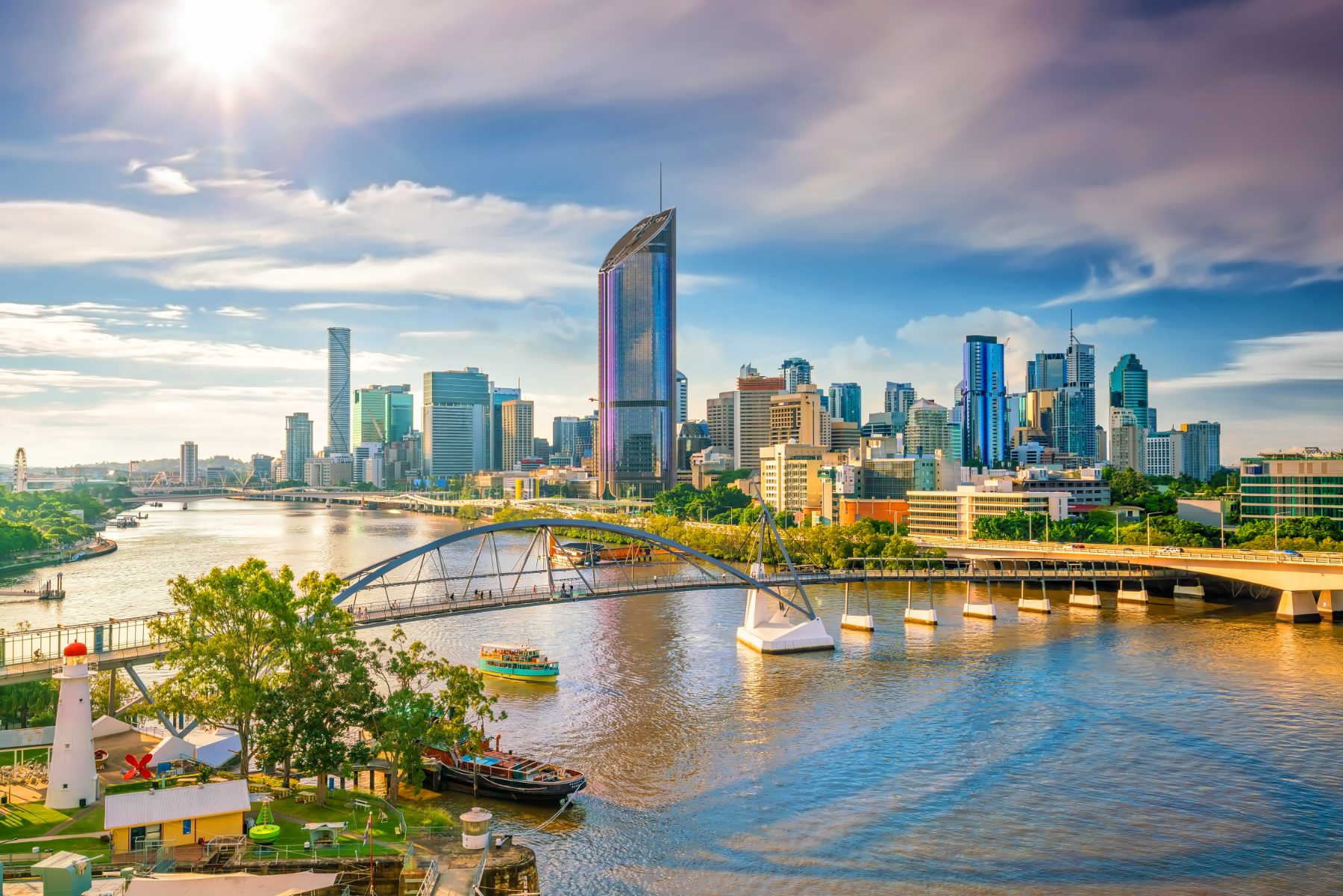 The Brisbane River at golden hour, the CBD skyline behind the Goodwill Bridge with a CityCat passing South Bank