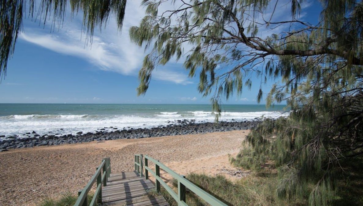 A timber boardwalk leading down through casuarina trees to a quiet beach on the Bundaberg coast