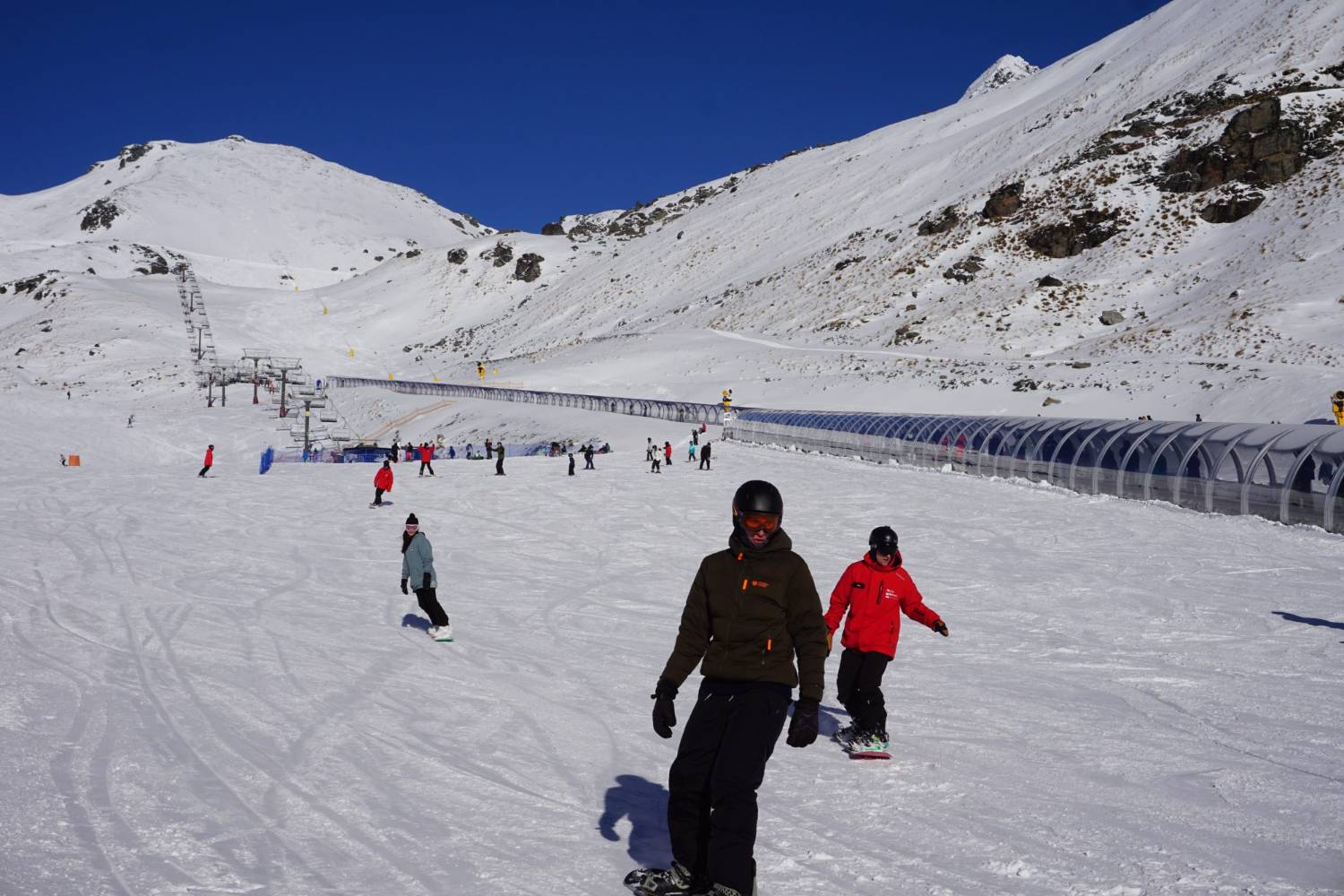 Skiers and snowboarders on a bright, snowy slope in the Southern Alps