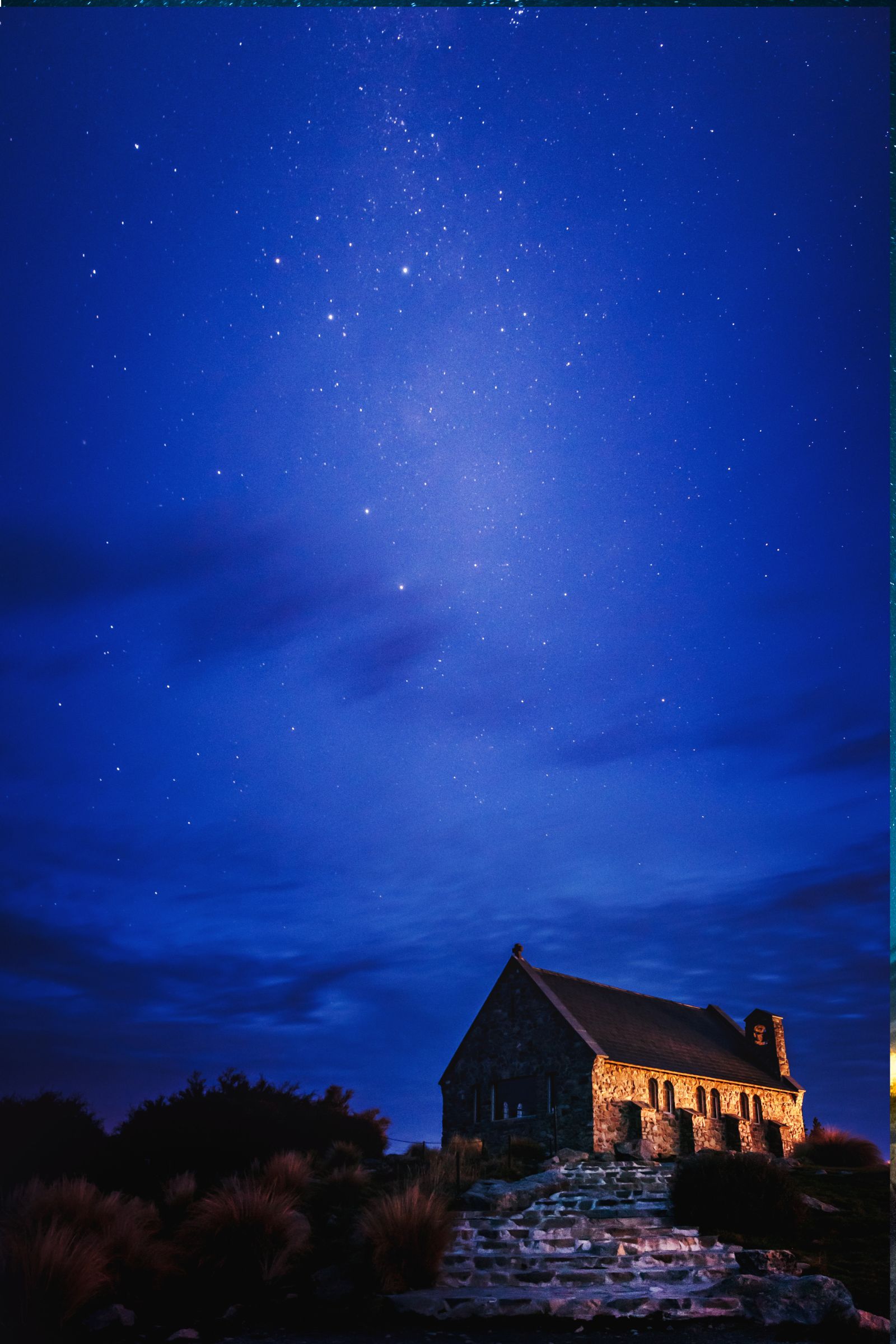 A small stone church under a night sky full of stars beside Lake Tekapo