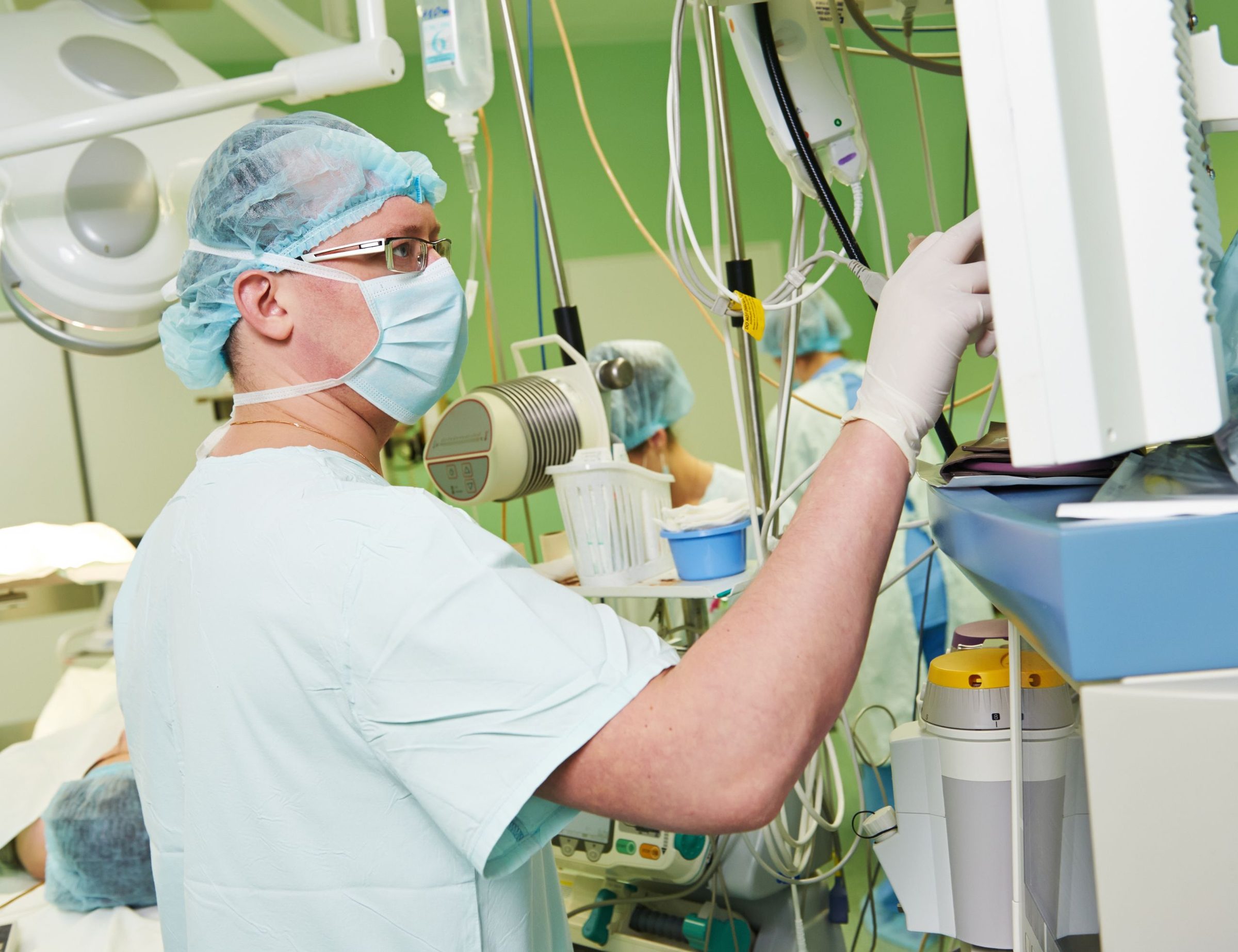 A clinician in theatre adjusting the anaesthetic machine beside a patient