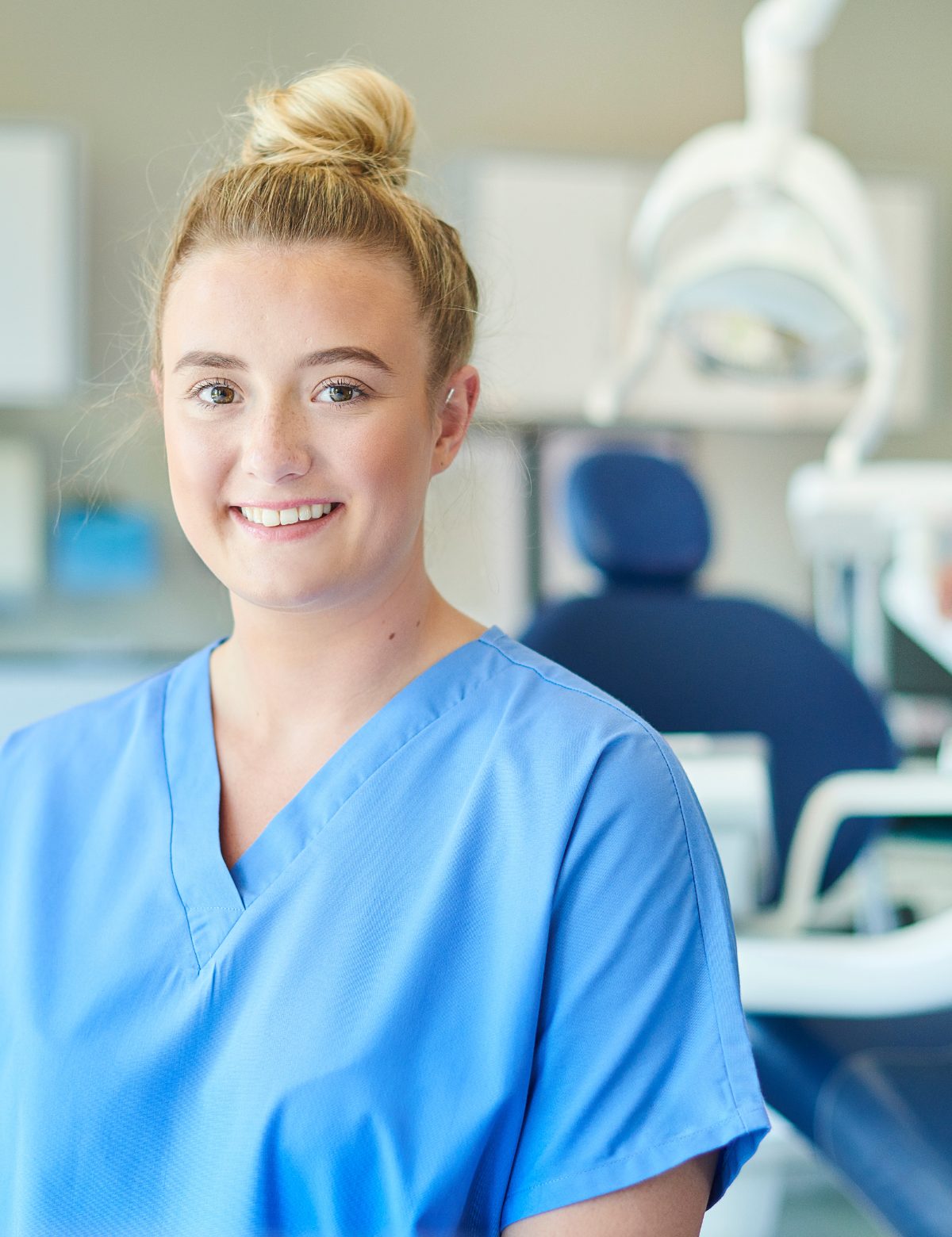 A smiling nurse in blue scrubs in a clinic