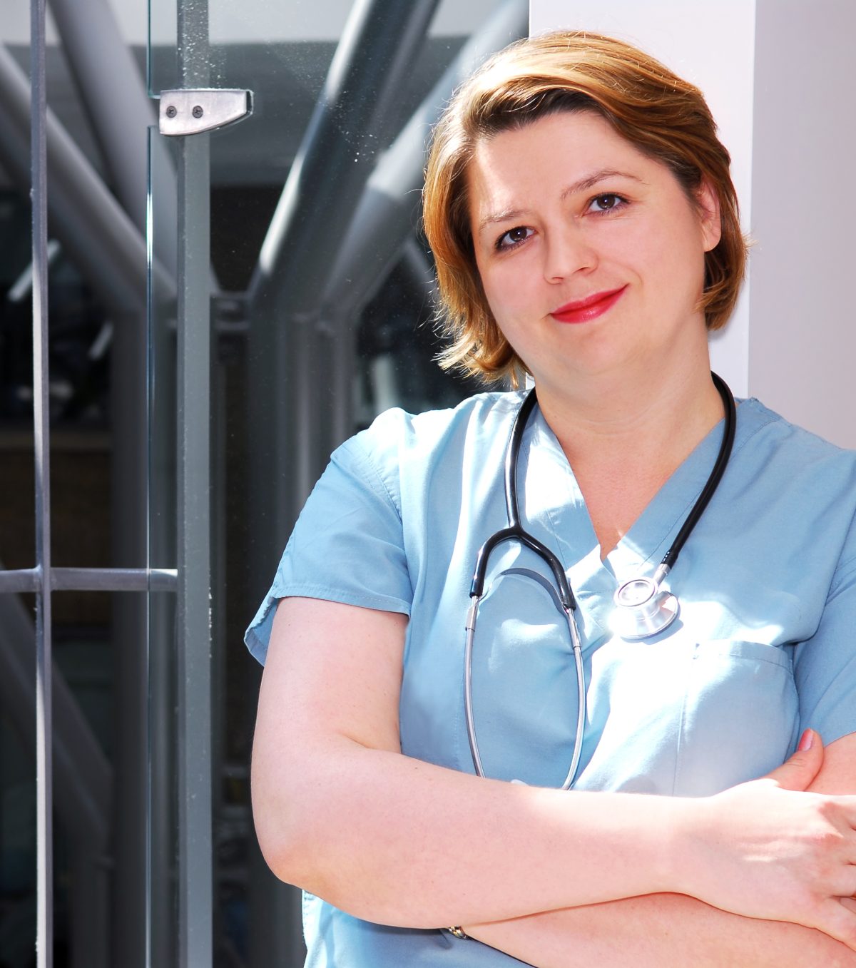 A clinician in scrubs with a stethoscope standing in a hospital corridor