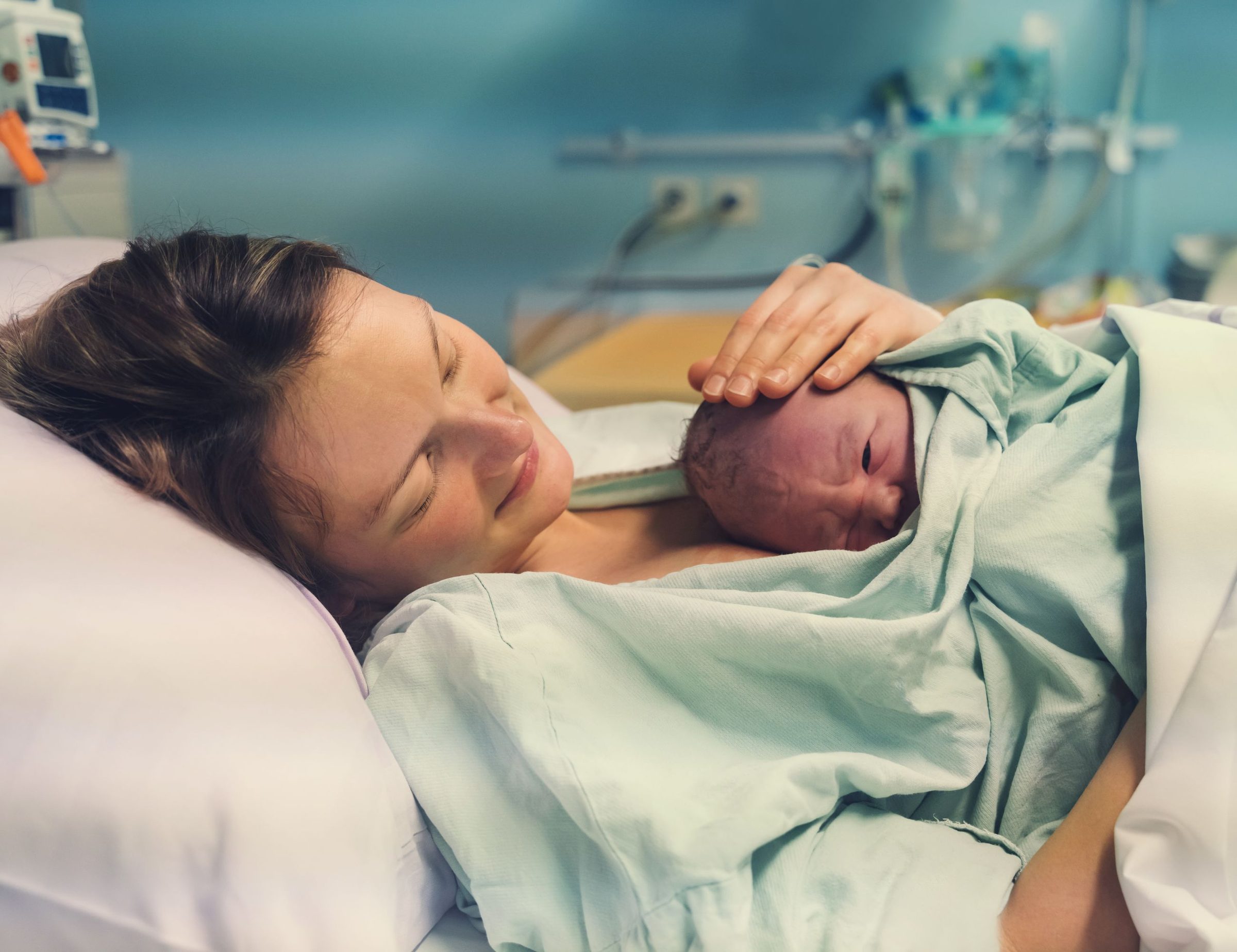 A mother holding her newborn baby against her chest in a hospital bed