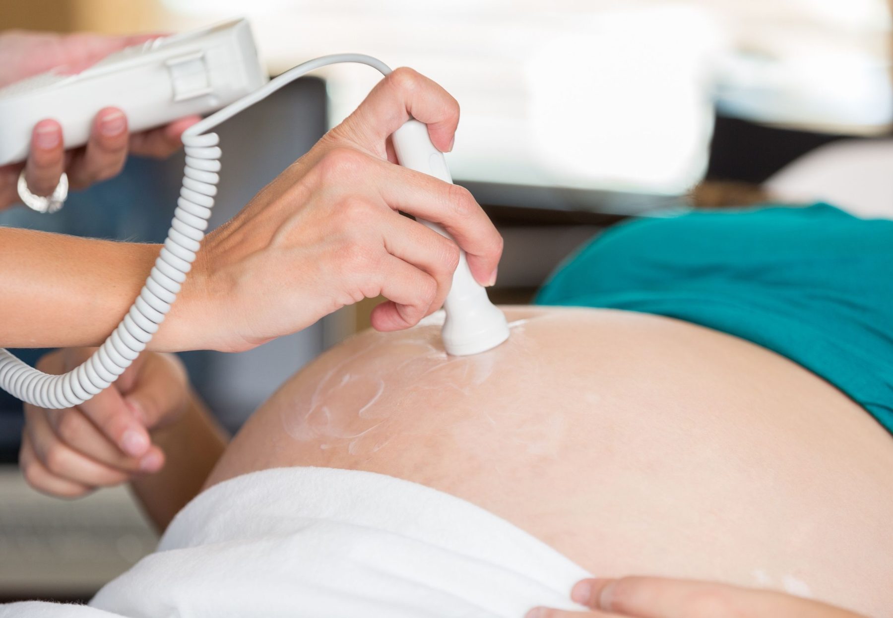 A sonographer holding an ultrasound probe on a pregnant patient's abdomen