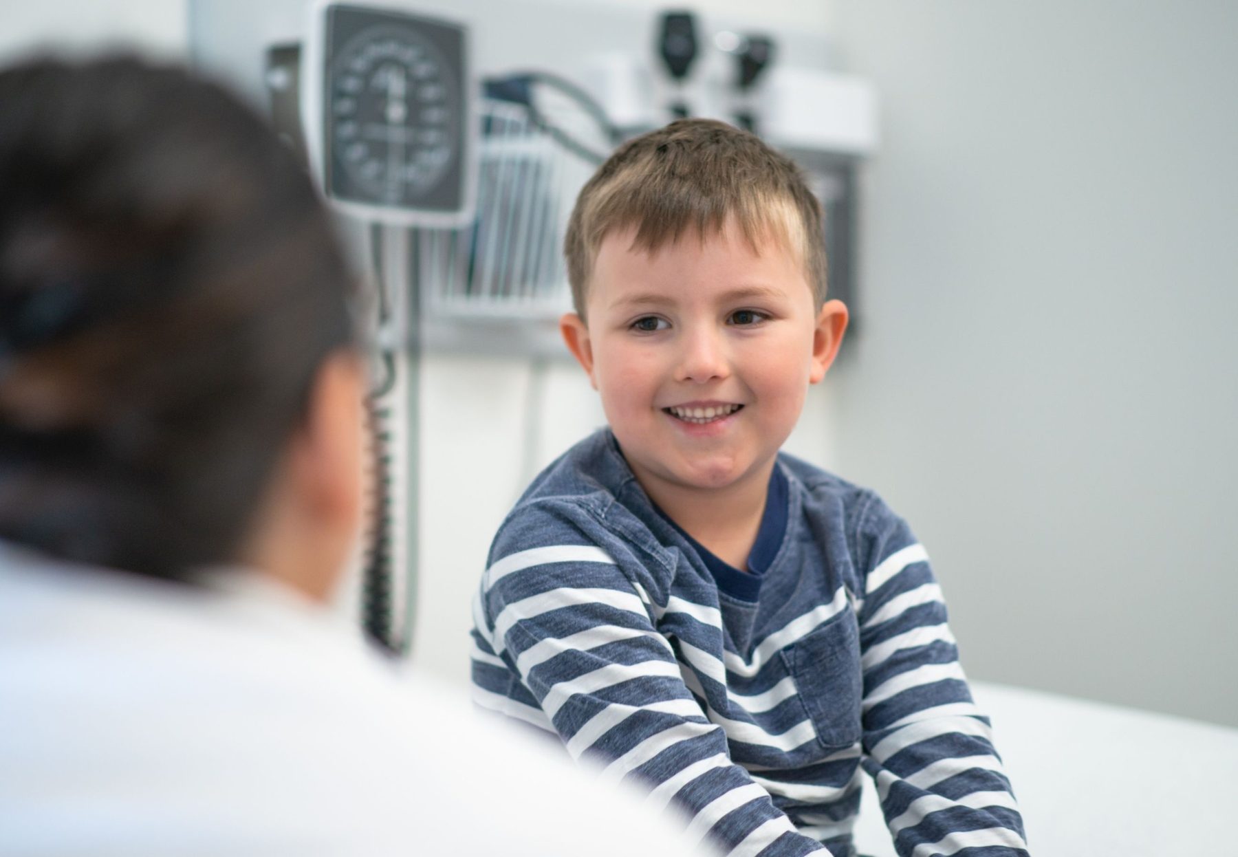 A smiling boy in a striped top talking with his paediatrician