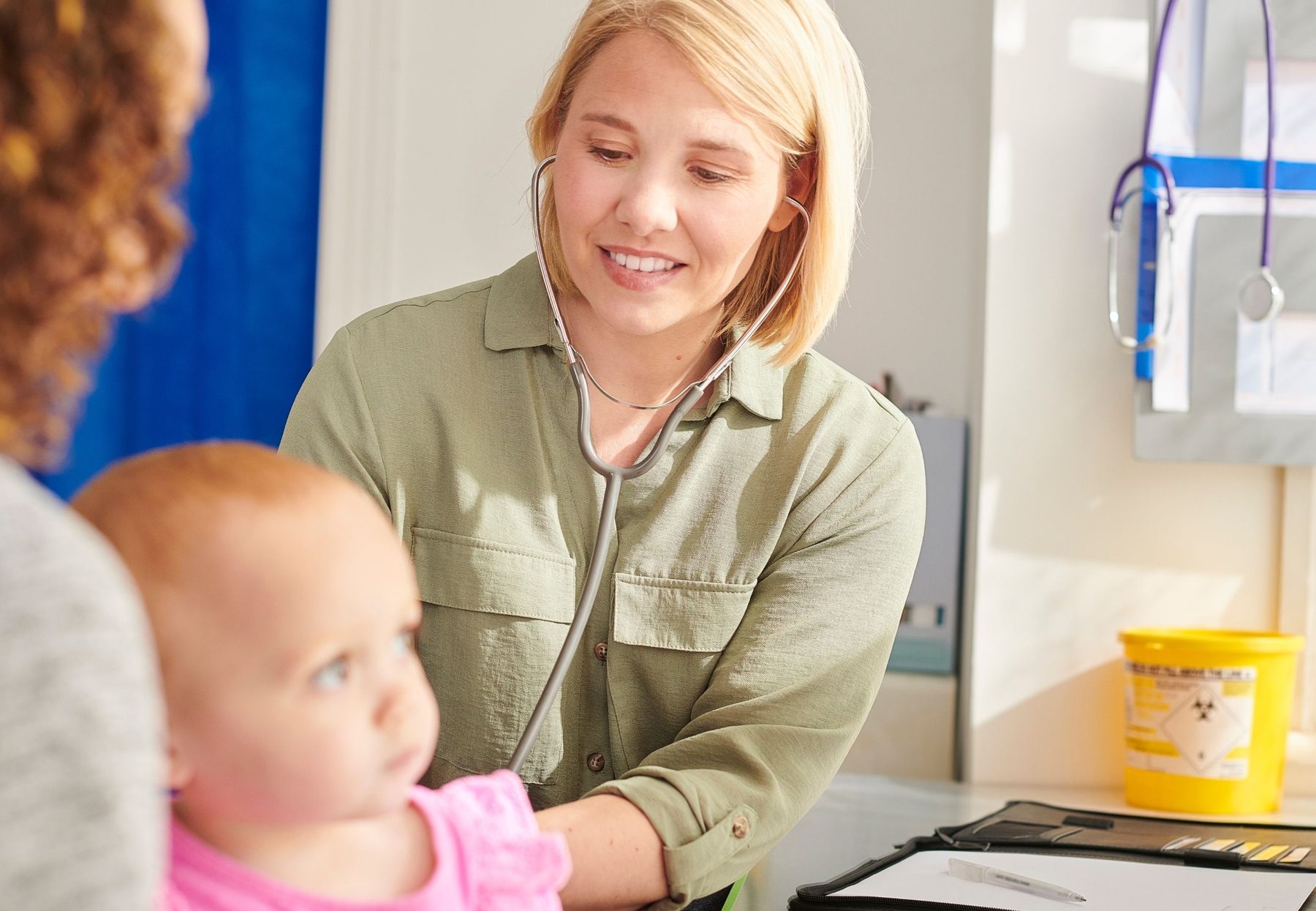 A paediatrician listening to a toddler&rsquo;s chest while a parent holds her