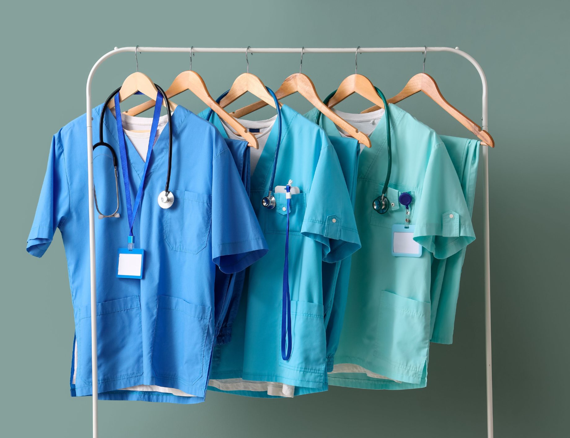 Sets of clinical scrubs on a rail with stethoscopes and blank ID badges