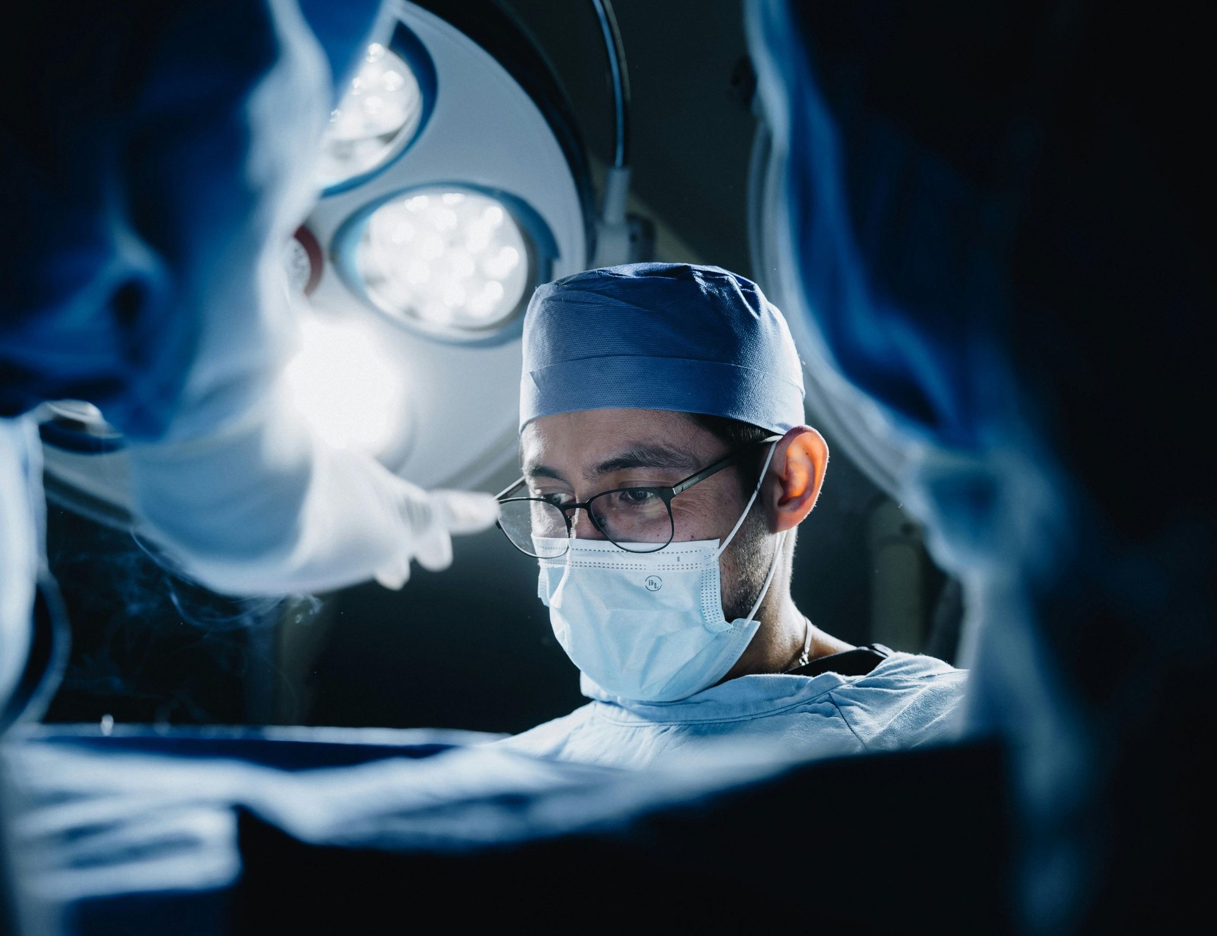 A clinician in cap and mask concentrating under procedure-room lights