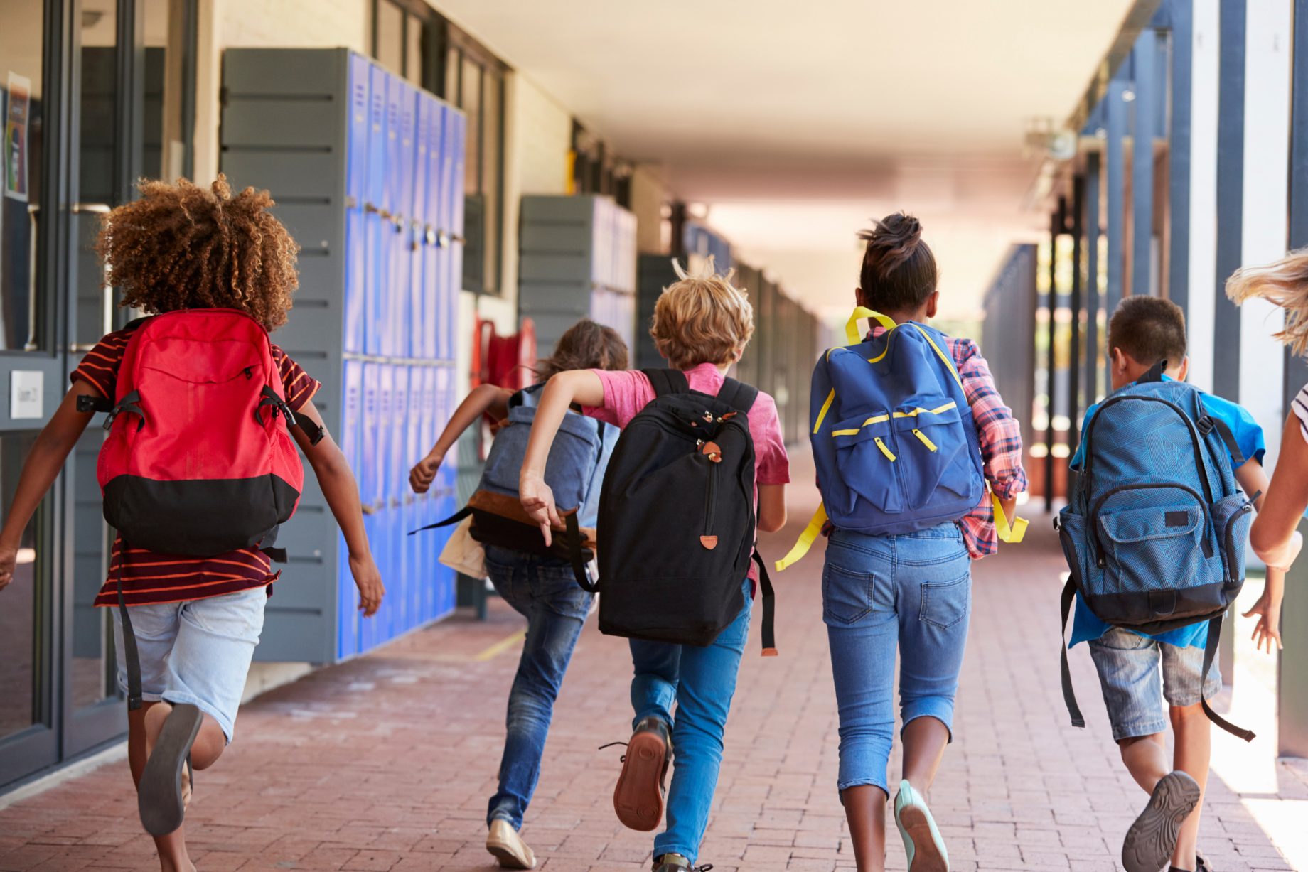 School students with backpacks running out along a covered walkway past lockers at the end of the day