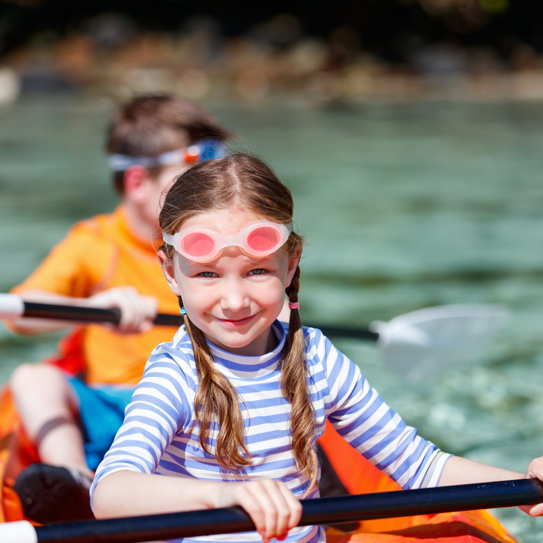 A child paddling a kayak on flat water, life jacket on, paddle mid-stroke