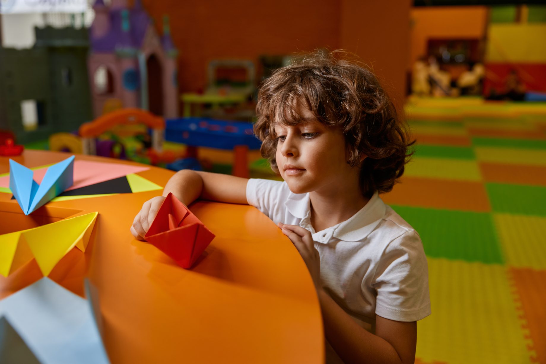 A child folding paper at a table in a holiday programme play room