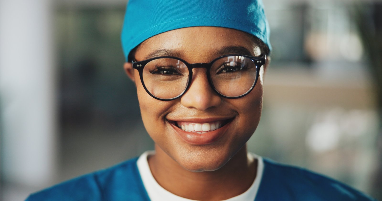 A smiling clinician in scrubs and a surgical cap