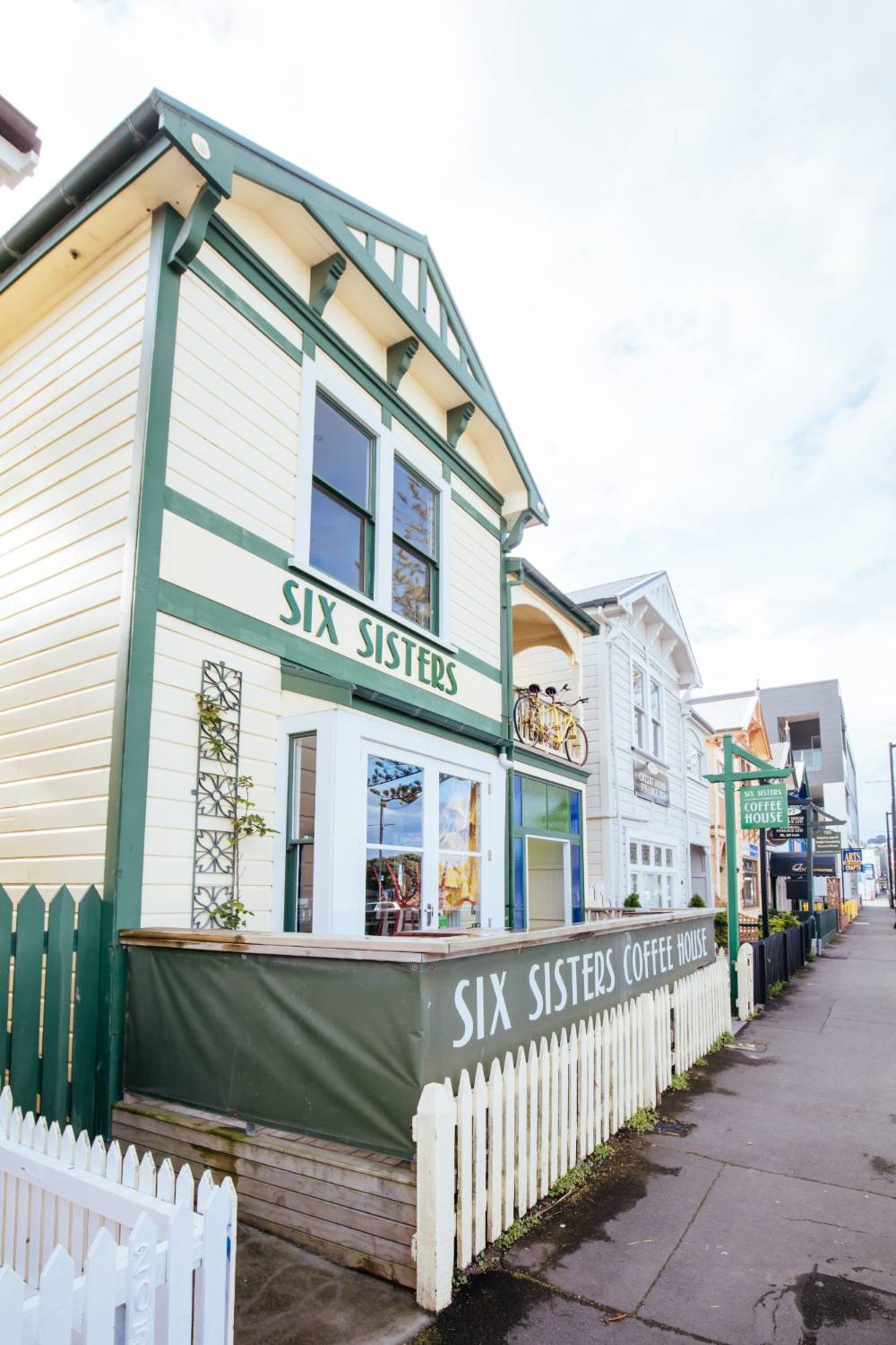 A cream weatherboard heritage building with dark green trim, housing a coffee house behind a white picket fence on a Napier street