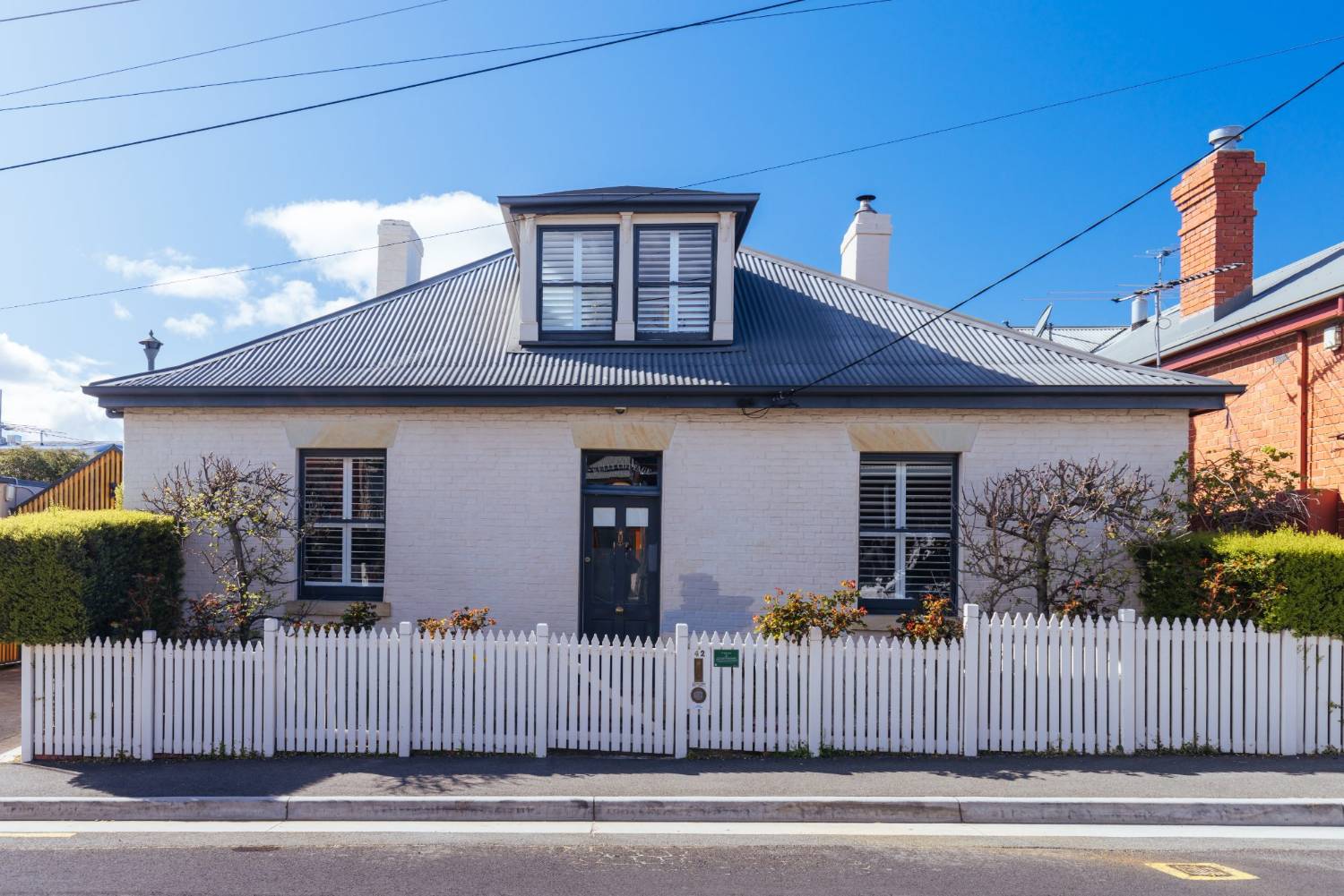 A restored white-painted colonial brick cottage with a picket fence in Battery Point, Hobart
