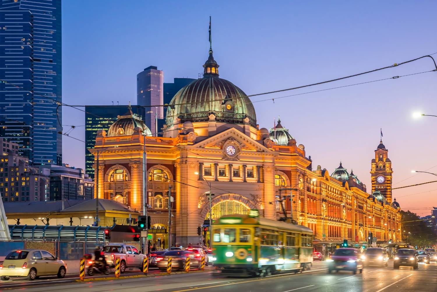 Flinders Street Station lit at dusk with a tram passing