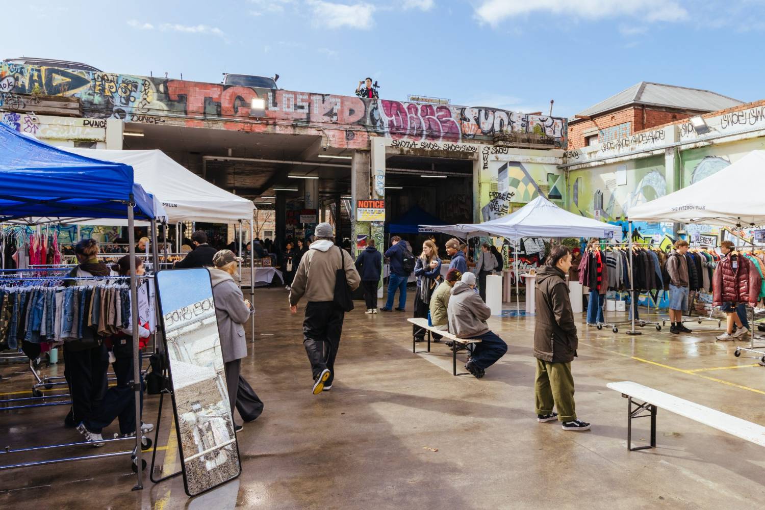 Racks of second-hand clothing under marquees in a graffitied yard at the Fitzroy Mills market