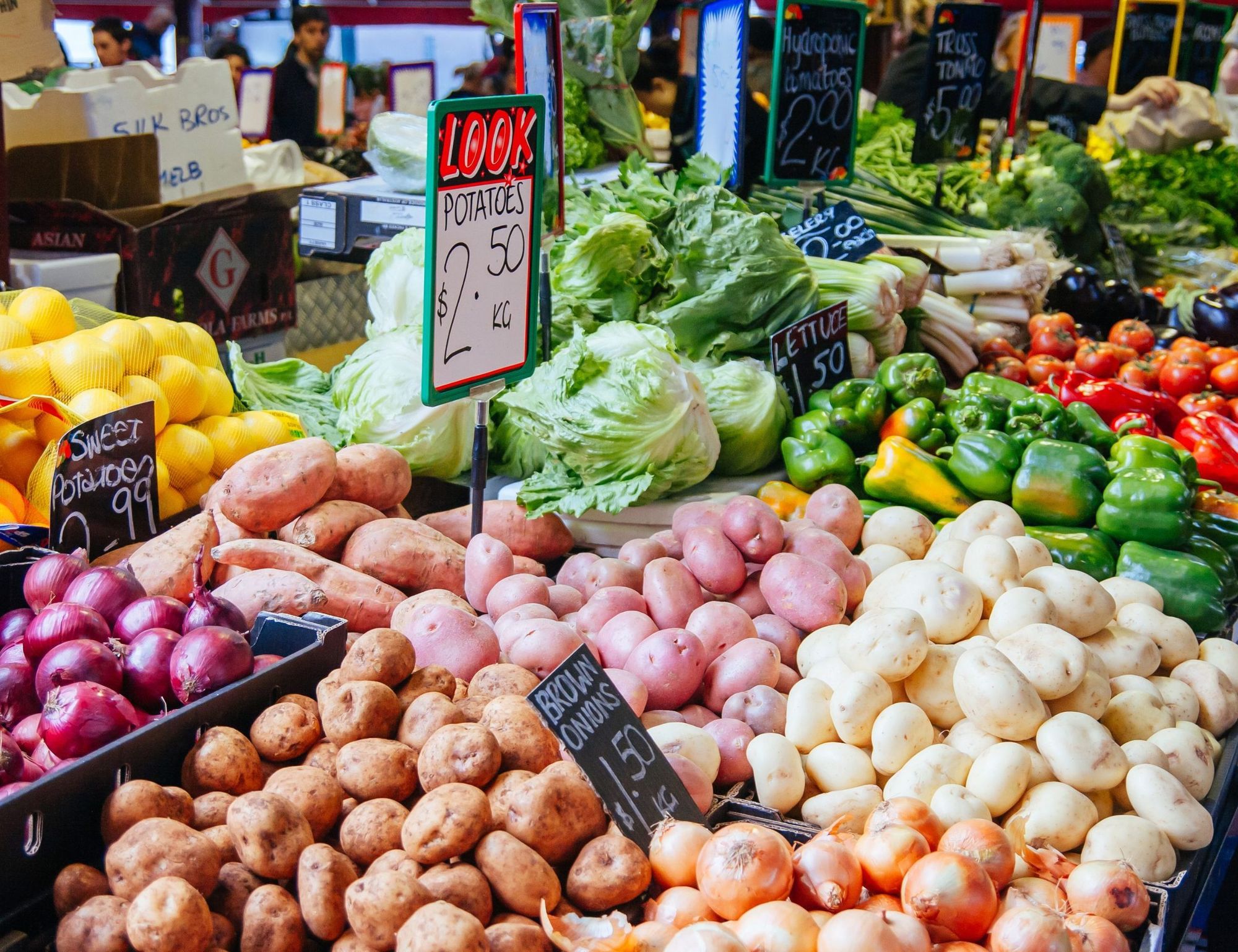 Fruit and vegetable stalls at Queen Victoria Market, potatoes, onions and capsicums under chalked price boards