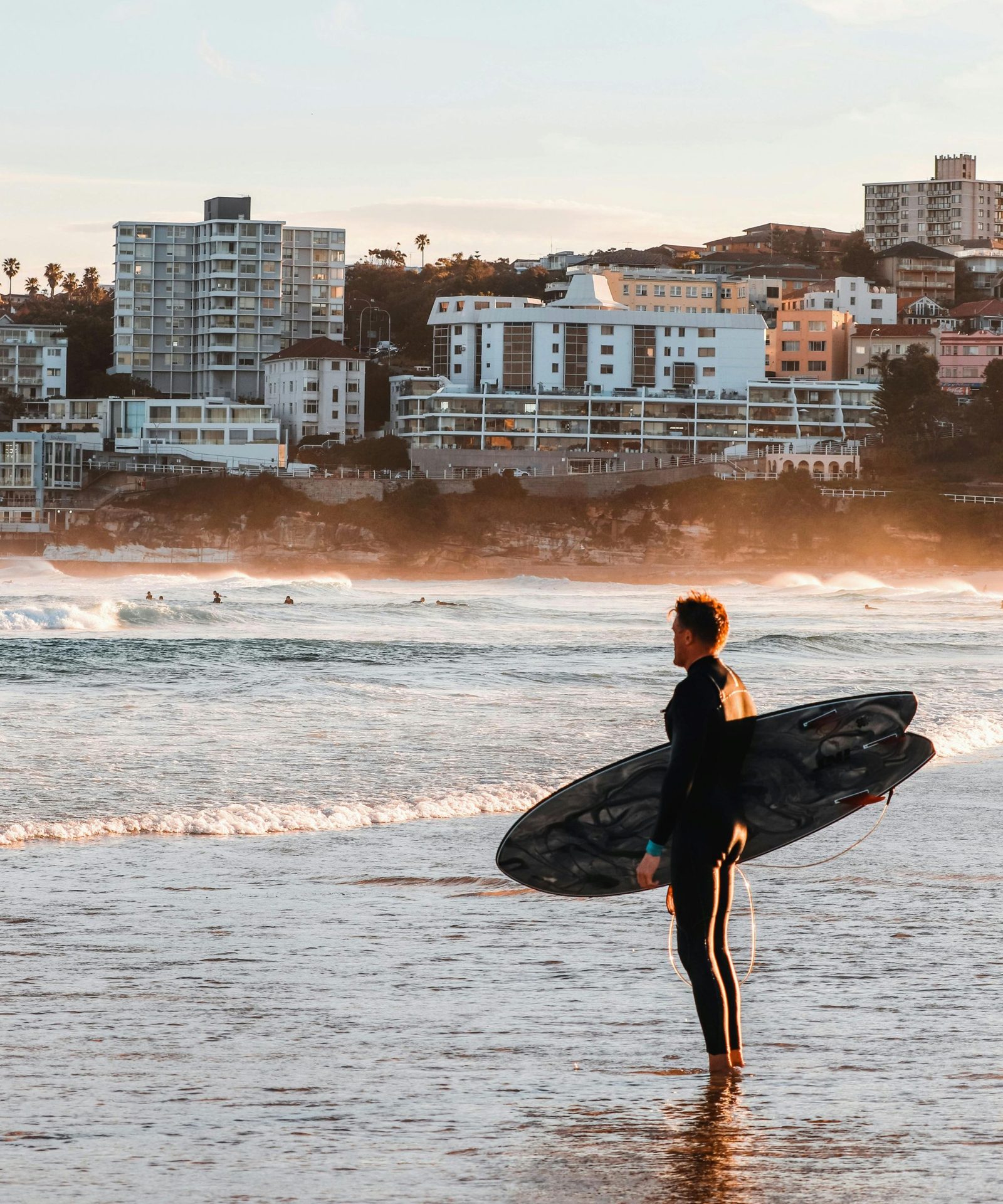 A surfer carrying a board into the water at Bondi at sunrise