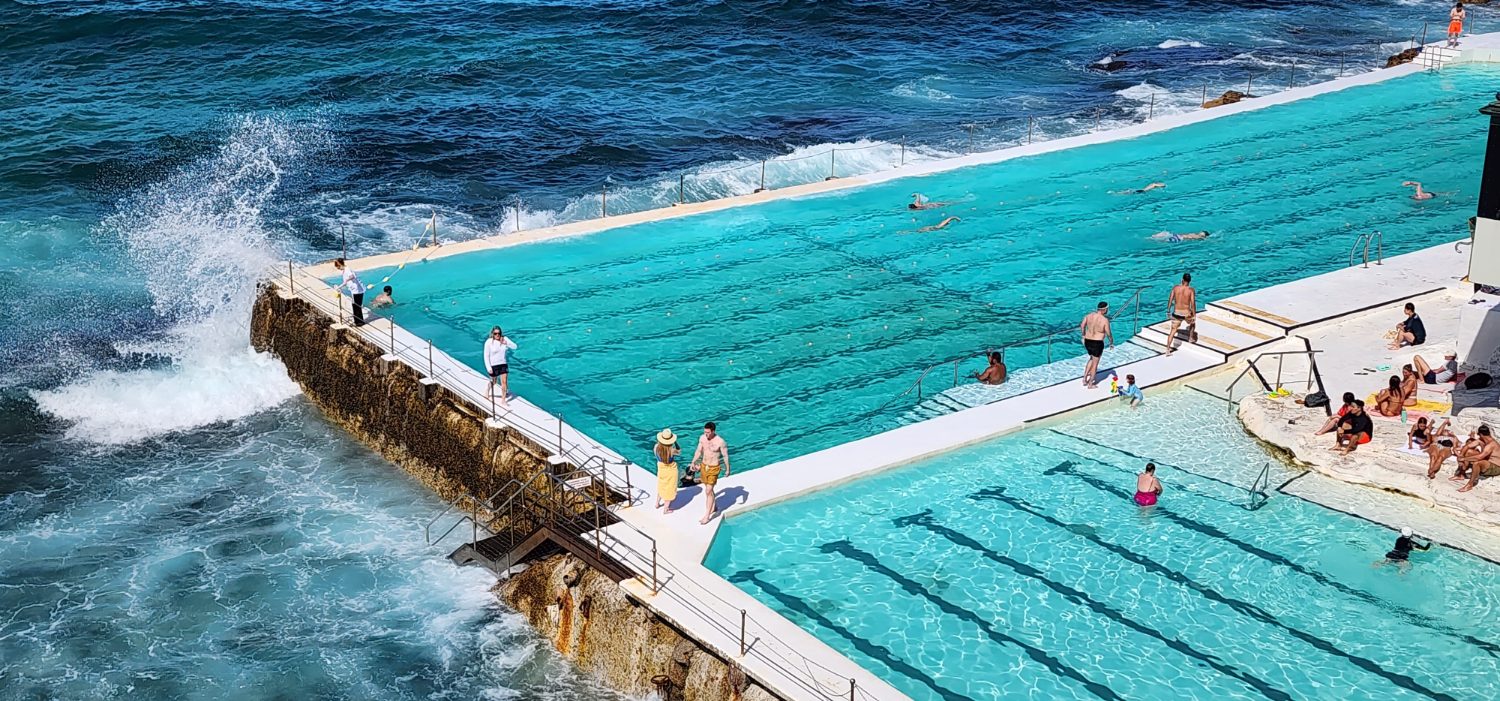 Swimmers in the ocean pool at Bondi Beach with waves breaking over the edge