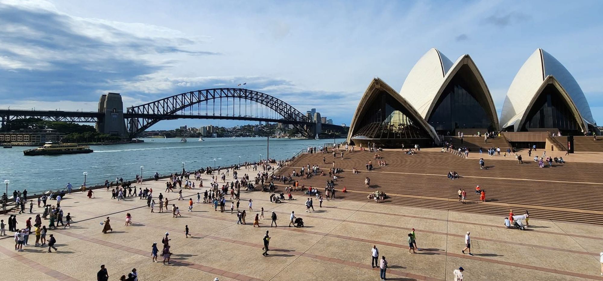 People on the harbour forecourt at Sydney, with the Opera House steps and the Harbour Bridge beyond