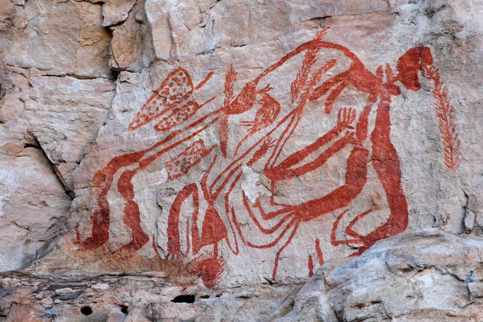 Red-ochre Aboriginal rock art figures painted on a sandstone wall in Kakadu