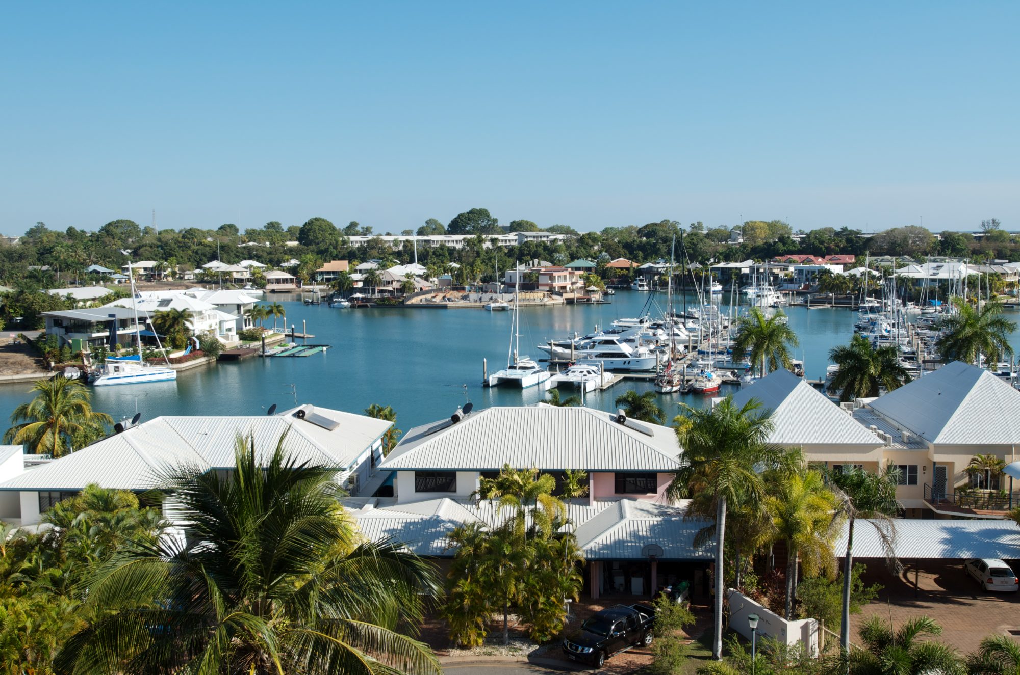 Marina-side housing in Darwin: white metal roofs, palms and moored yachts on a still morning