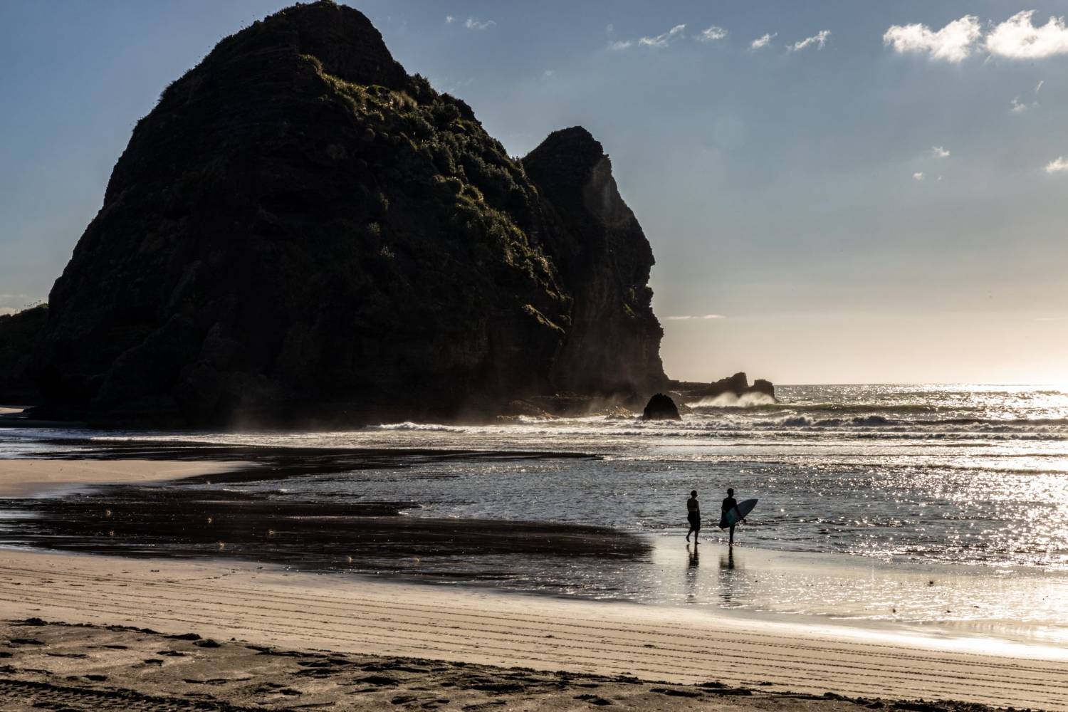 Surfers walking out at Piha with Lion Rock behind them