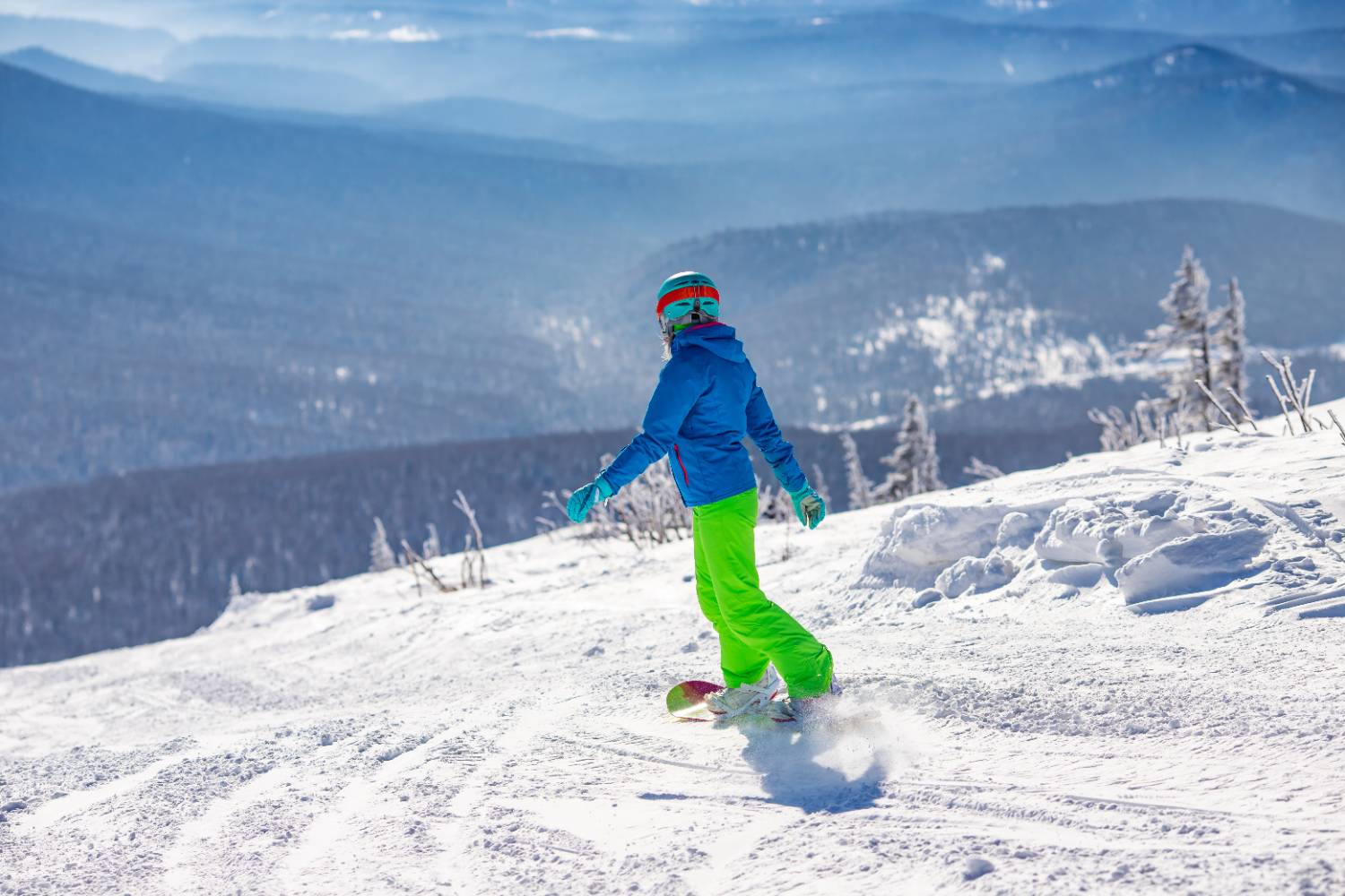 A snowboarder carving down a sunny slope above a valley