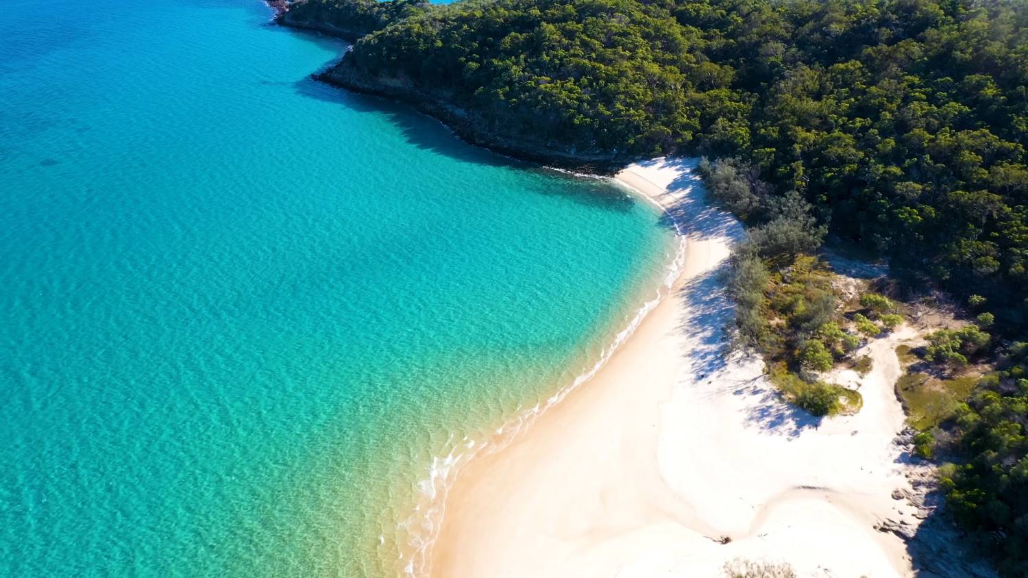 A quiet Australian coastline, turquoise water meeting white sand and bushland