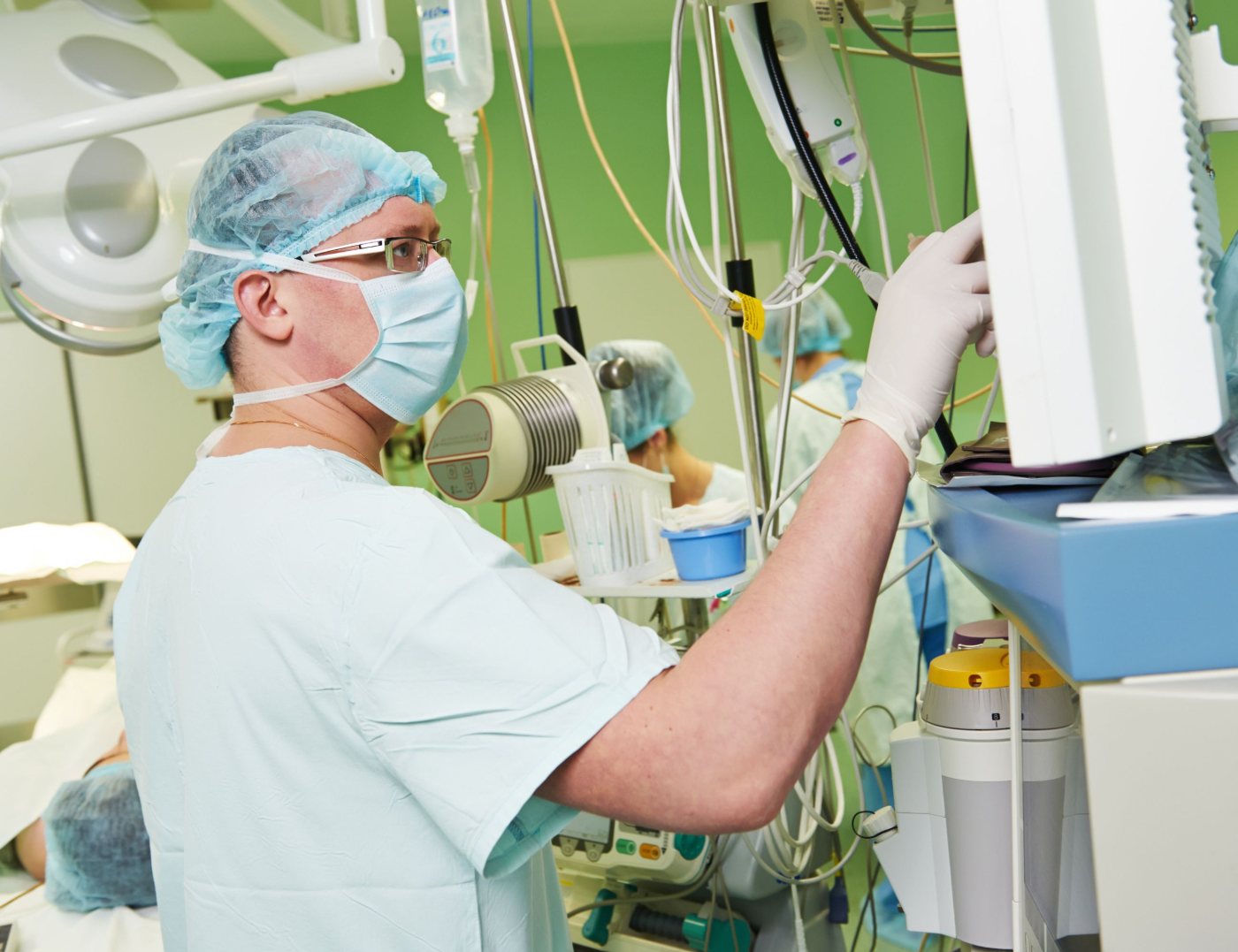 An anaesthetic technician adjusting monitoring equipment beside the operating table