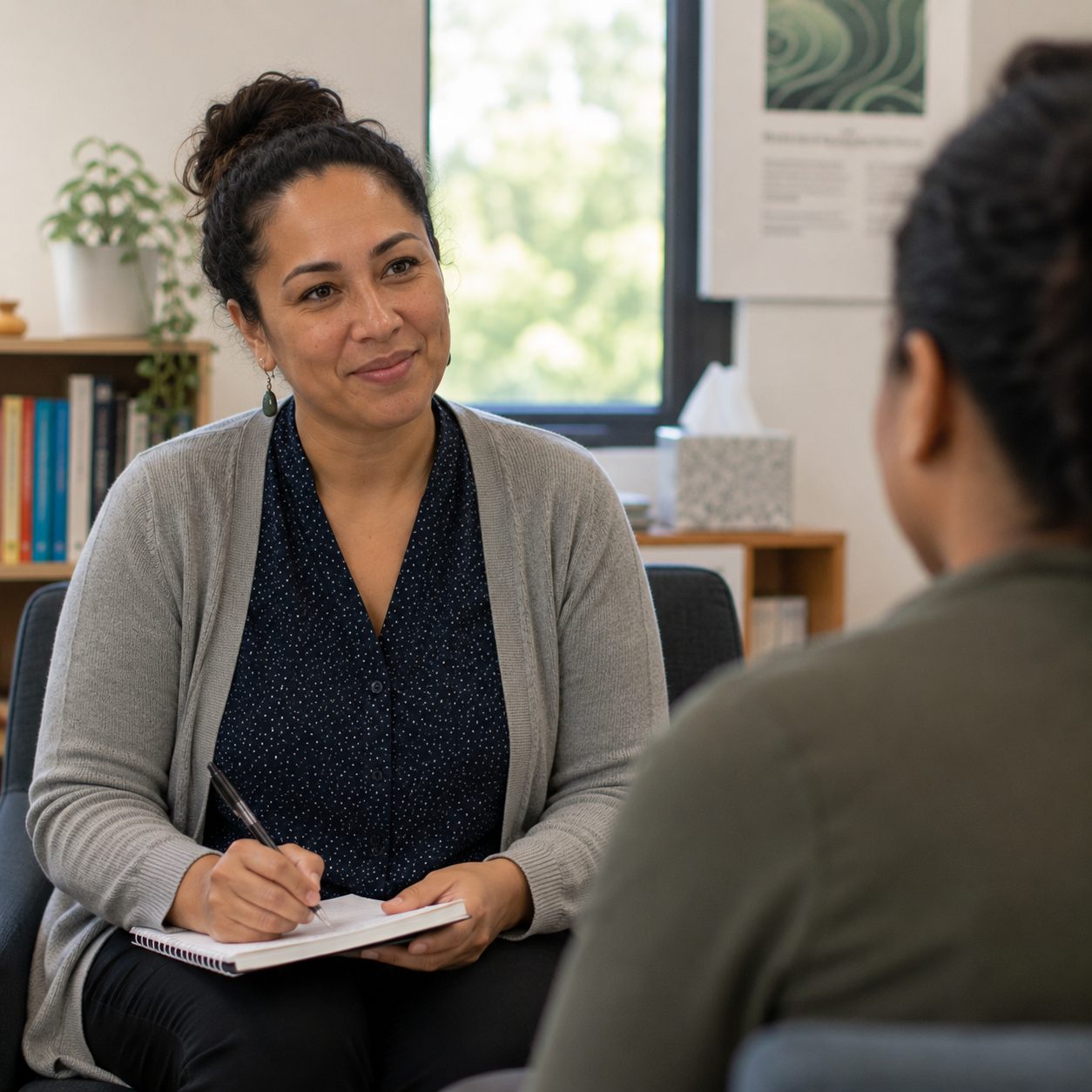 A clinician with a notebook listening to a client in a consulting room
