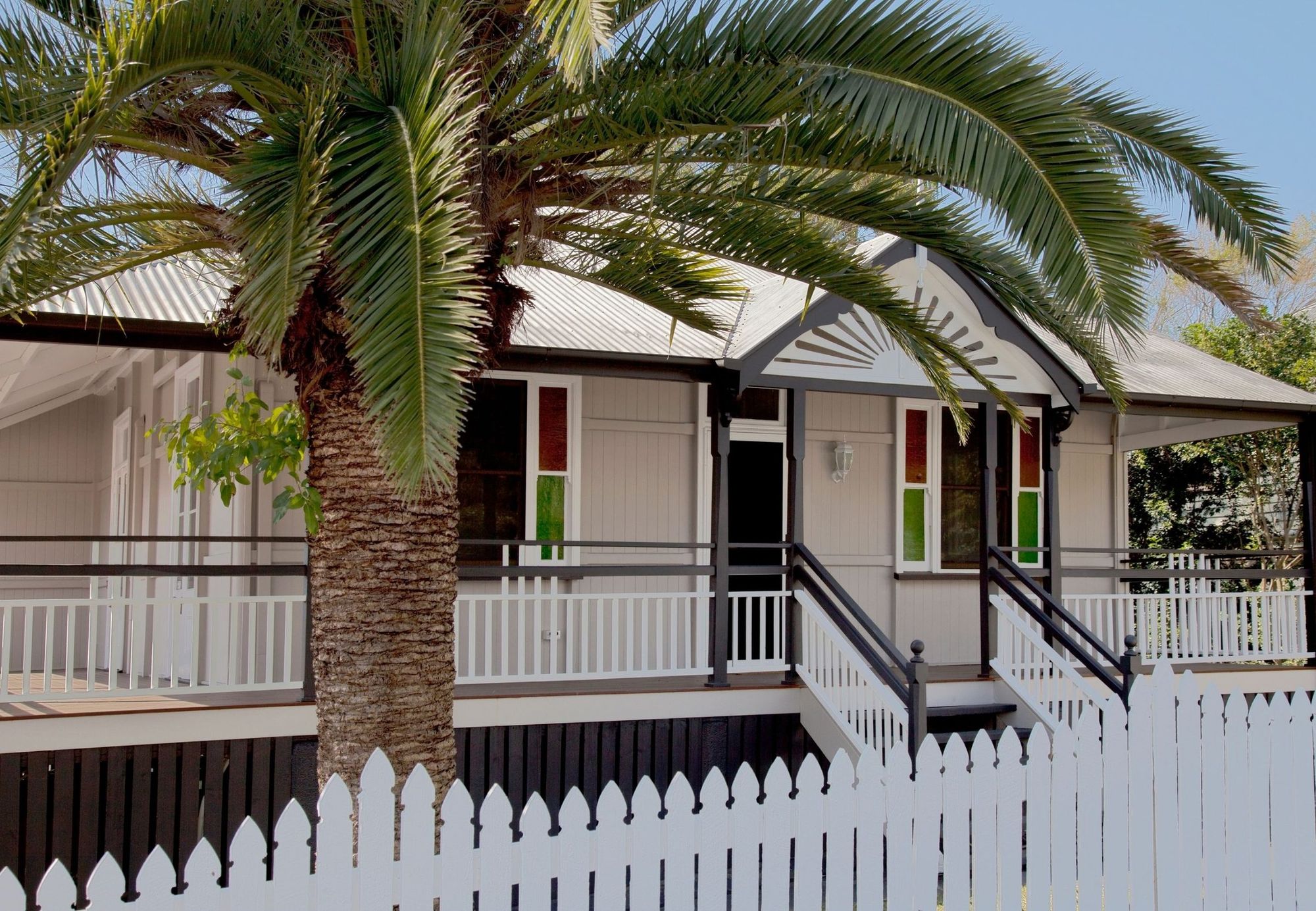 A traditional Queenslander house with a verandah, white picket fence and a palm in the front garden