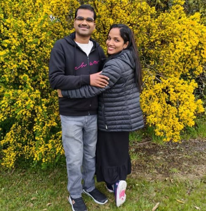 Anu and her husband smiling in front of a bank of yellow flowering gorse