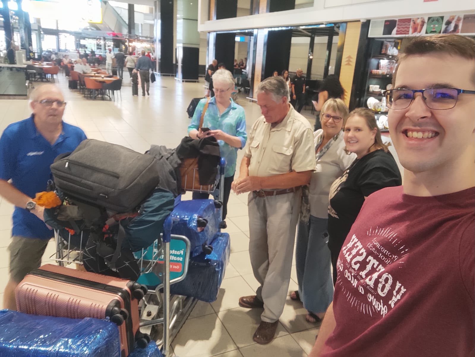 Janita and Jonathan with family gathered around a luggage trolley at the airport before their flight