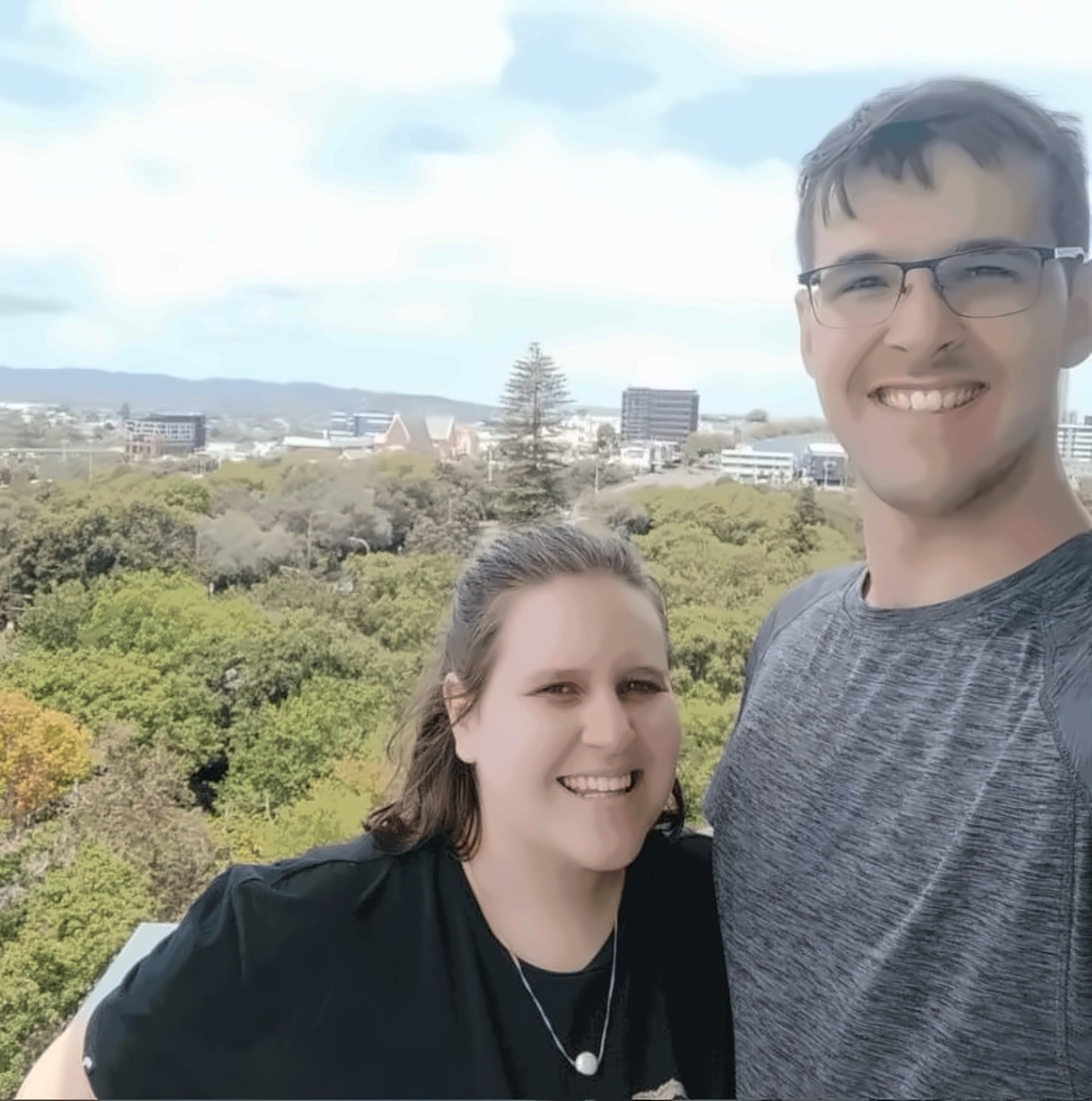 Janita and Jonathan on a lookout, a wide canopy of trees and low city buildings spread out behind them