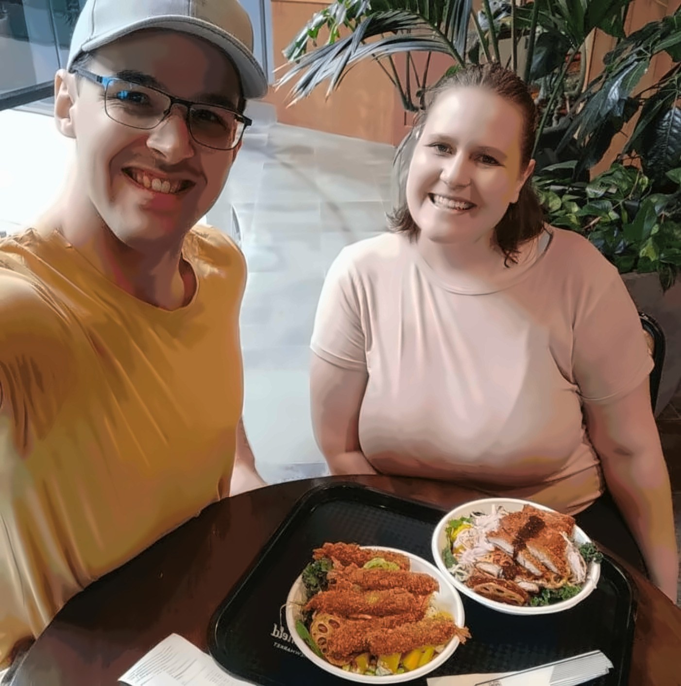 Janita and Jonathan at a table with a tray of two katsu rice bowls between them