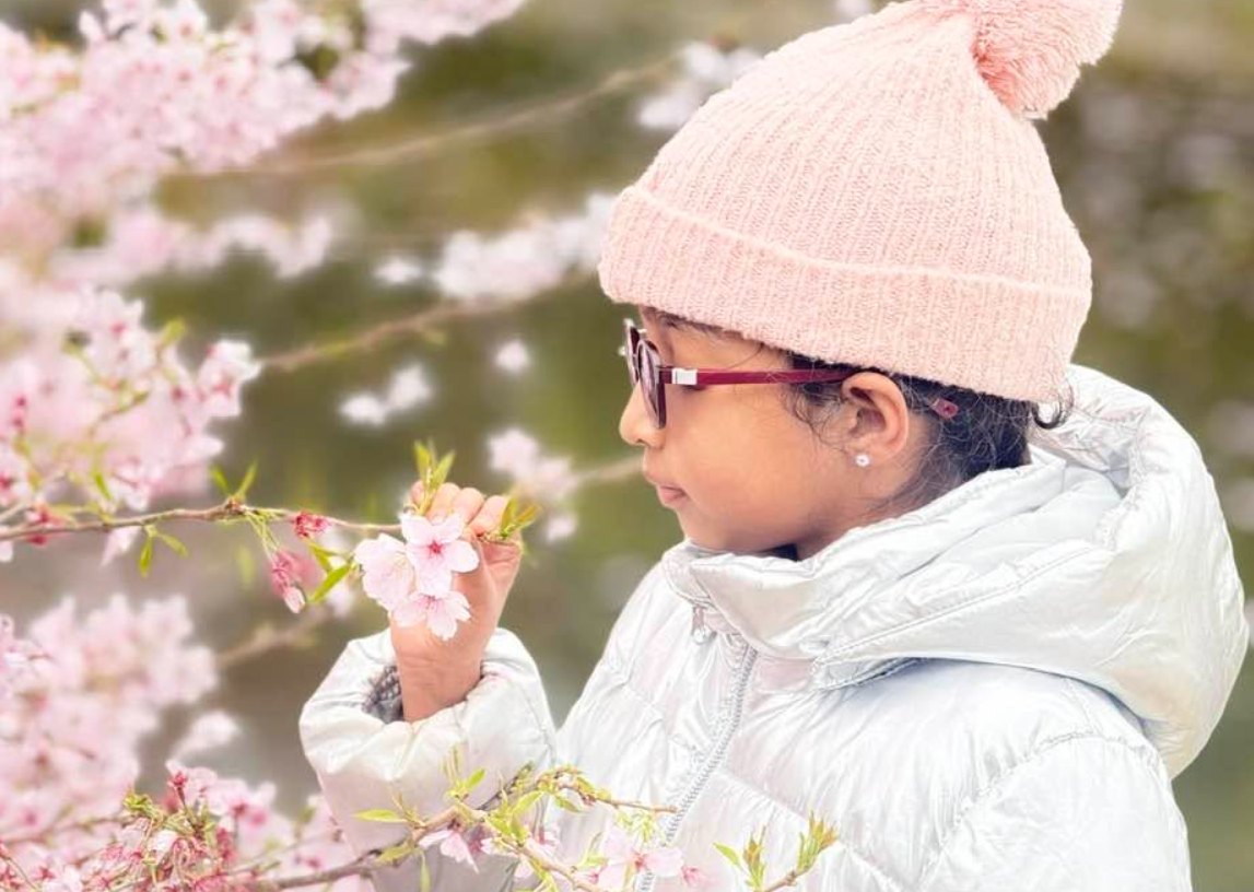 Neethu&rsquo;s daughter in a pink beanie holding a sprig of cherry blossom