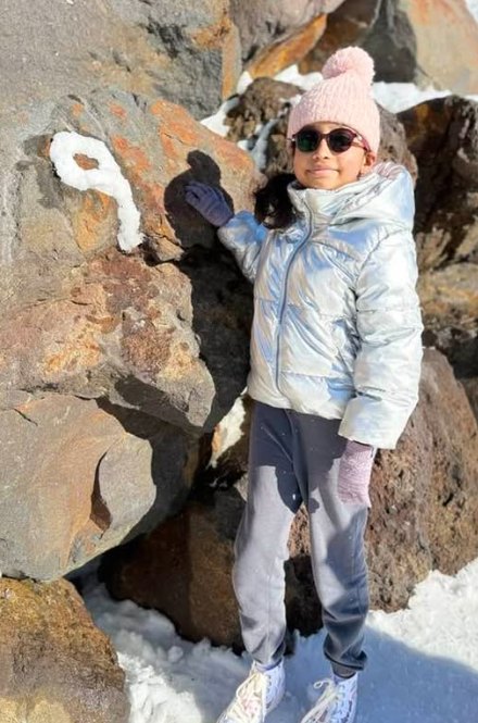Neethu&rsquo;s daughter in a silver puffer jacket and pink beanie by snowy rocks