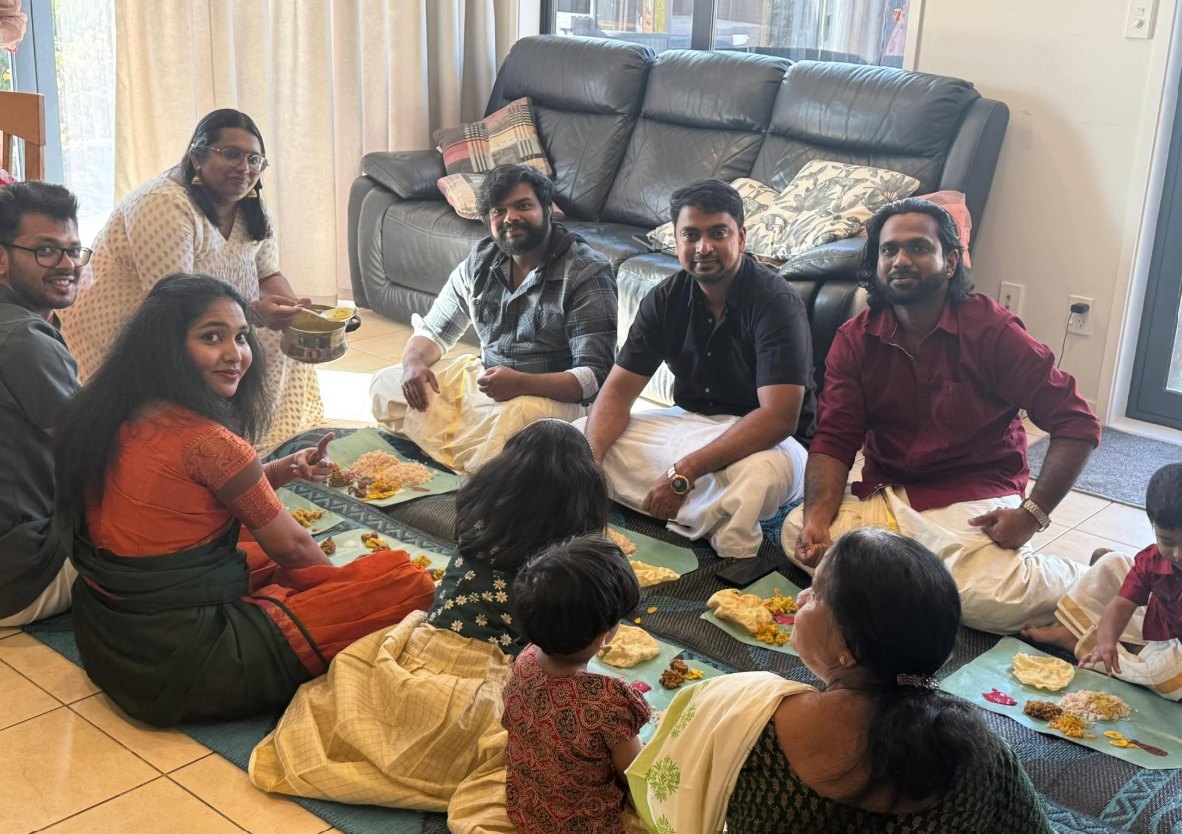 Friends and their families sitting on the living-room floor for an Onam sadya served on banana leaves