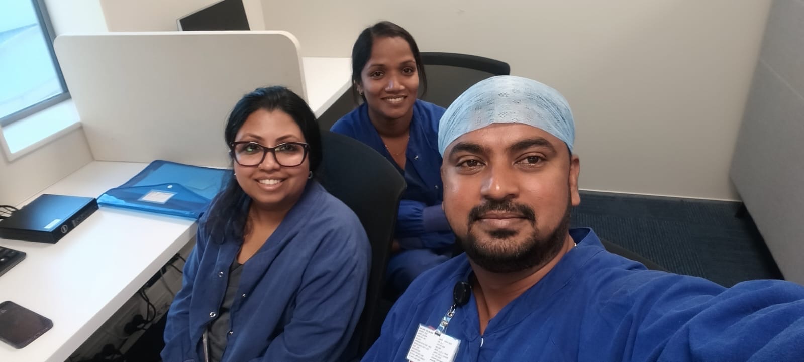 Three anaesthetic technicians in blue theatre scrubs smiling together at work