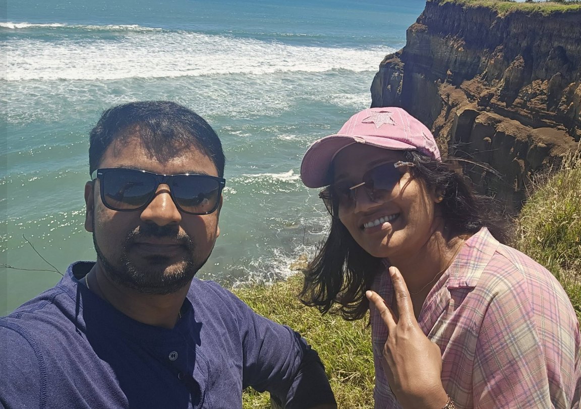 Rezon and his wife smiling for a selfie on a clifftop above the sea in New Zealand