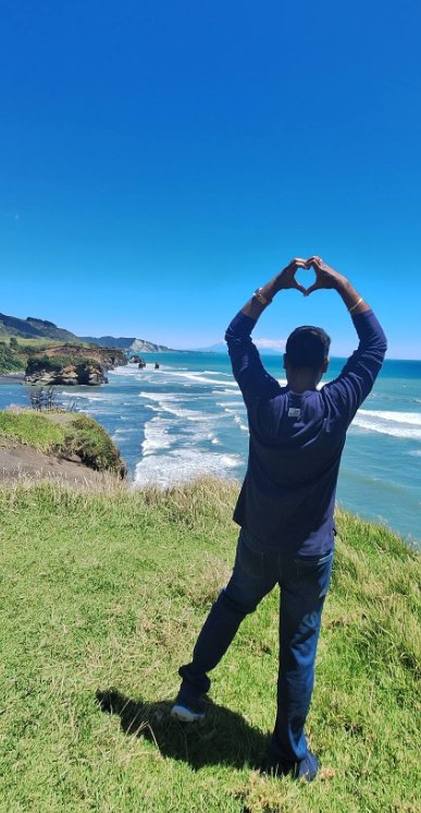 Rezon making a heart shape with his hands above a wild coastline