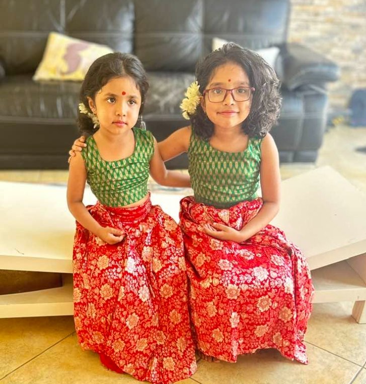 Two young sisters in matching green and red silk outfits with jasmine in their hair