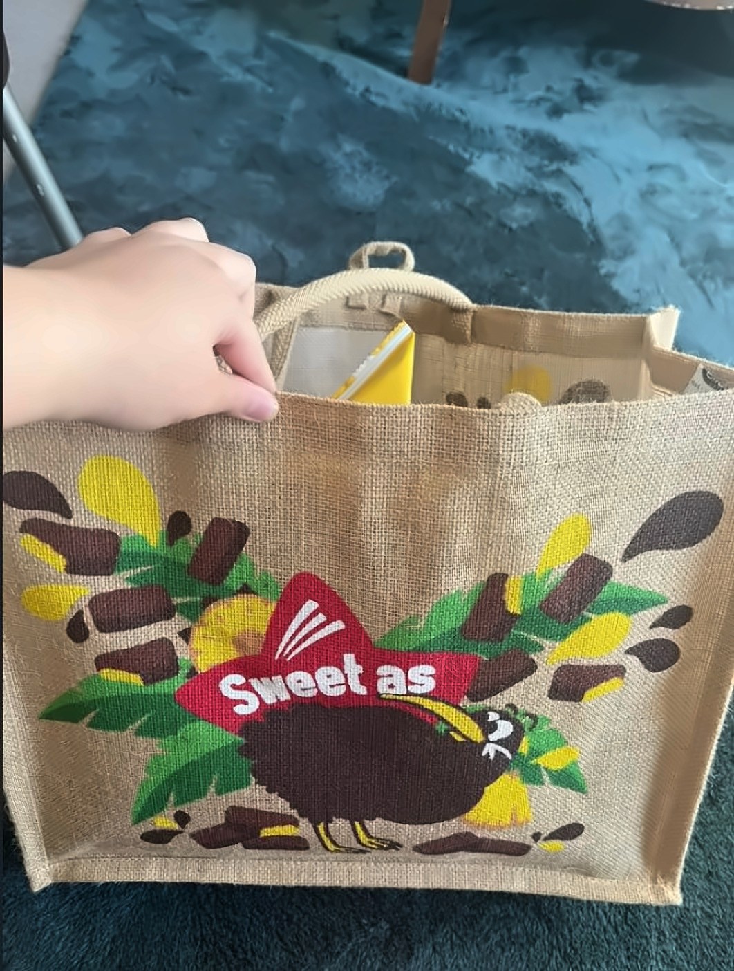 Janita opening a jute bag printed with a kiwi and the words Sweet as, a card tucked inside